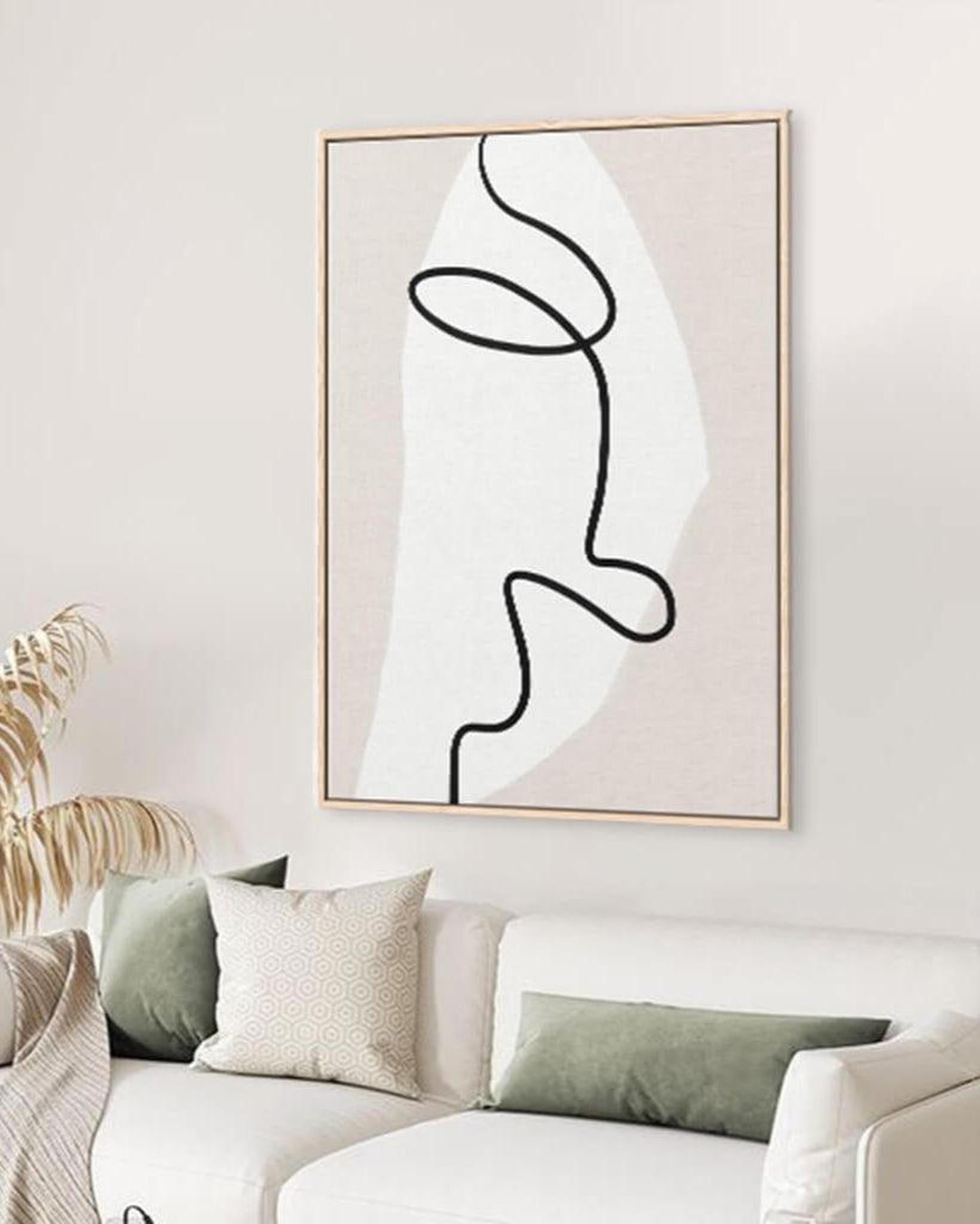 Abstract line art of a face in a gold frame on a wall above a sofa.