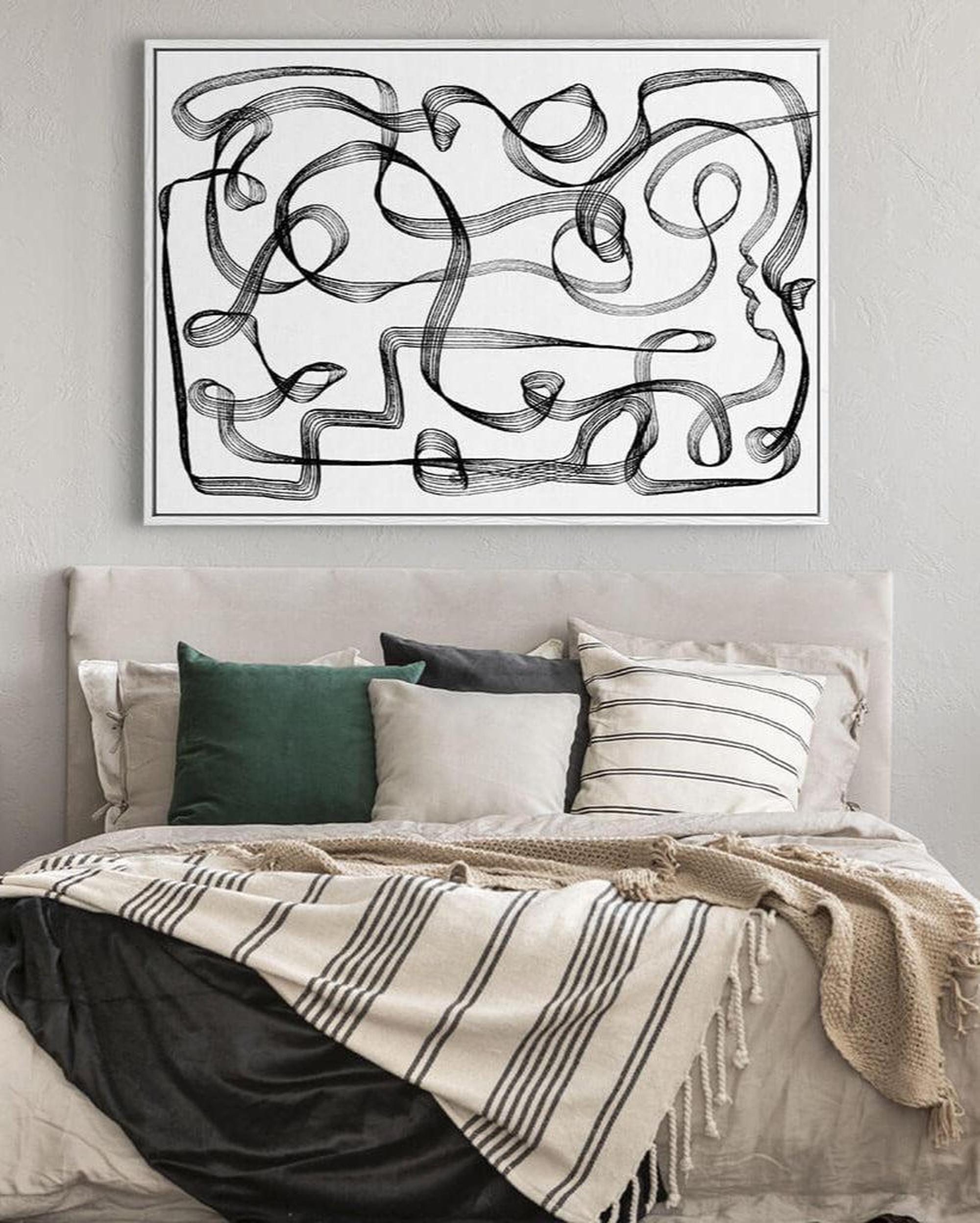 Abstract black and white artwork on a wall above a bed with pillows and blankets.