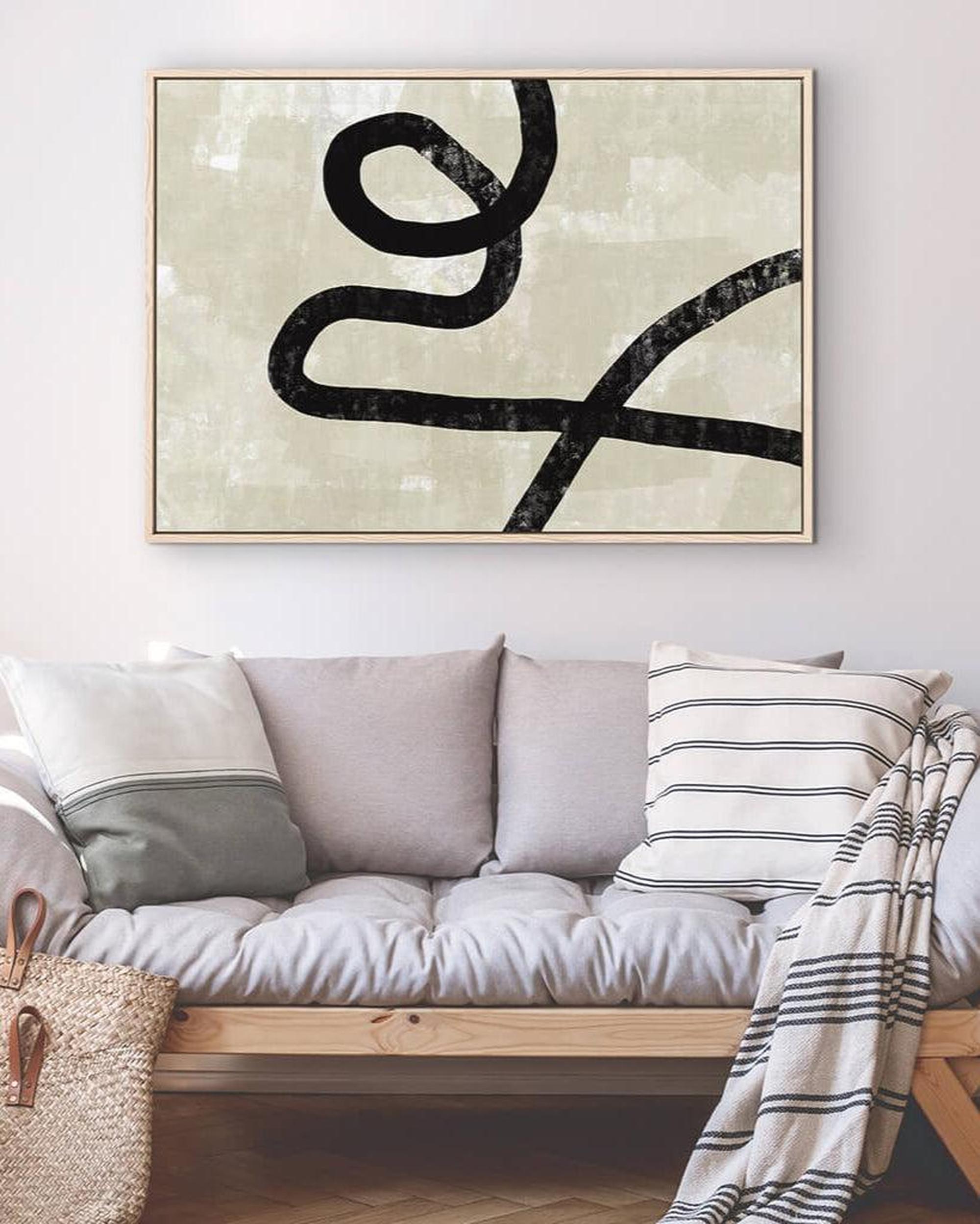 Abstract black line art on a light background above a sofa with decorative pillows and a blanket.