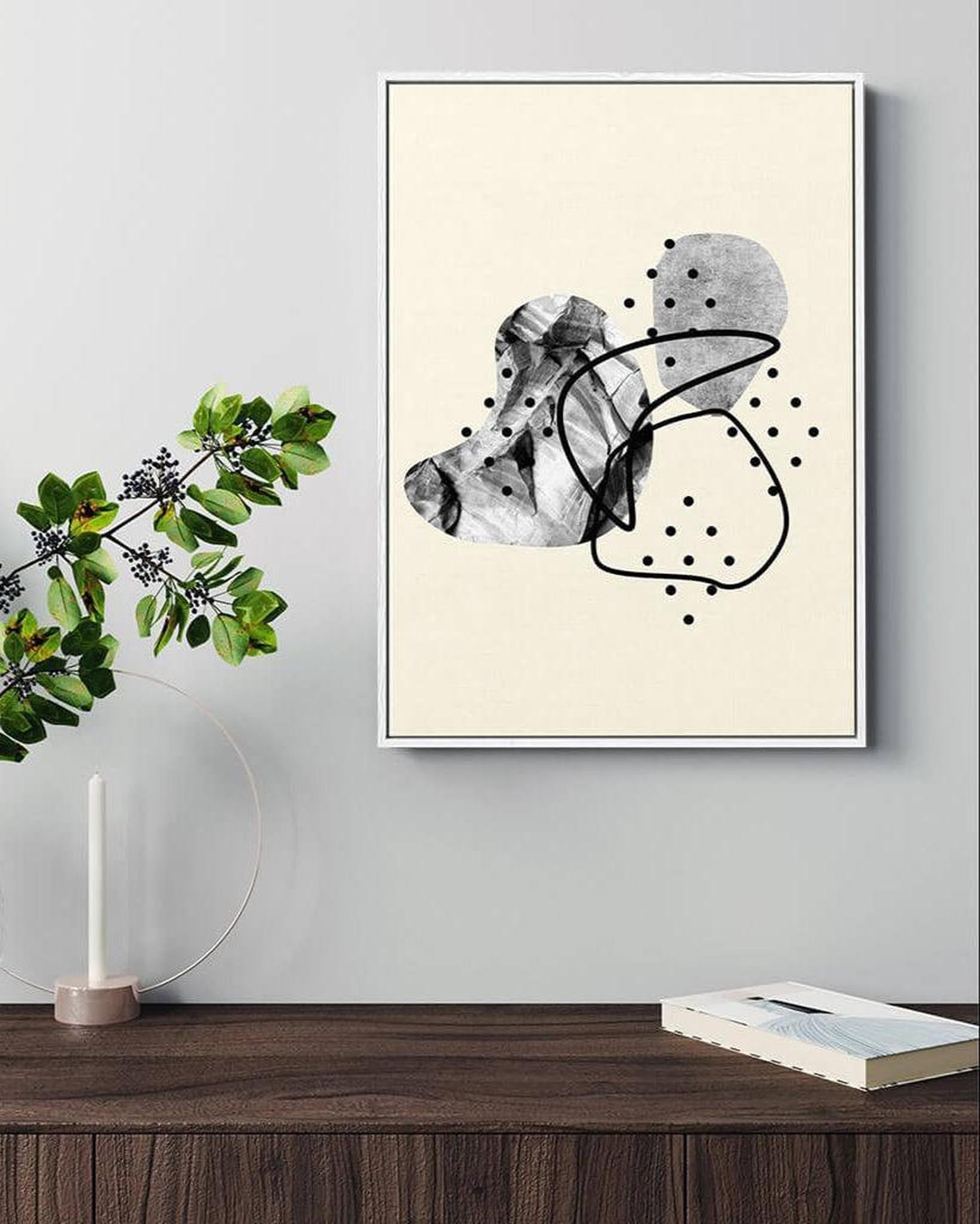 Framed abstract art piece on a wall above a wooden surface with a plant and book.