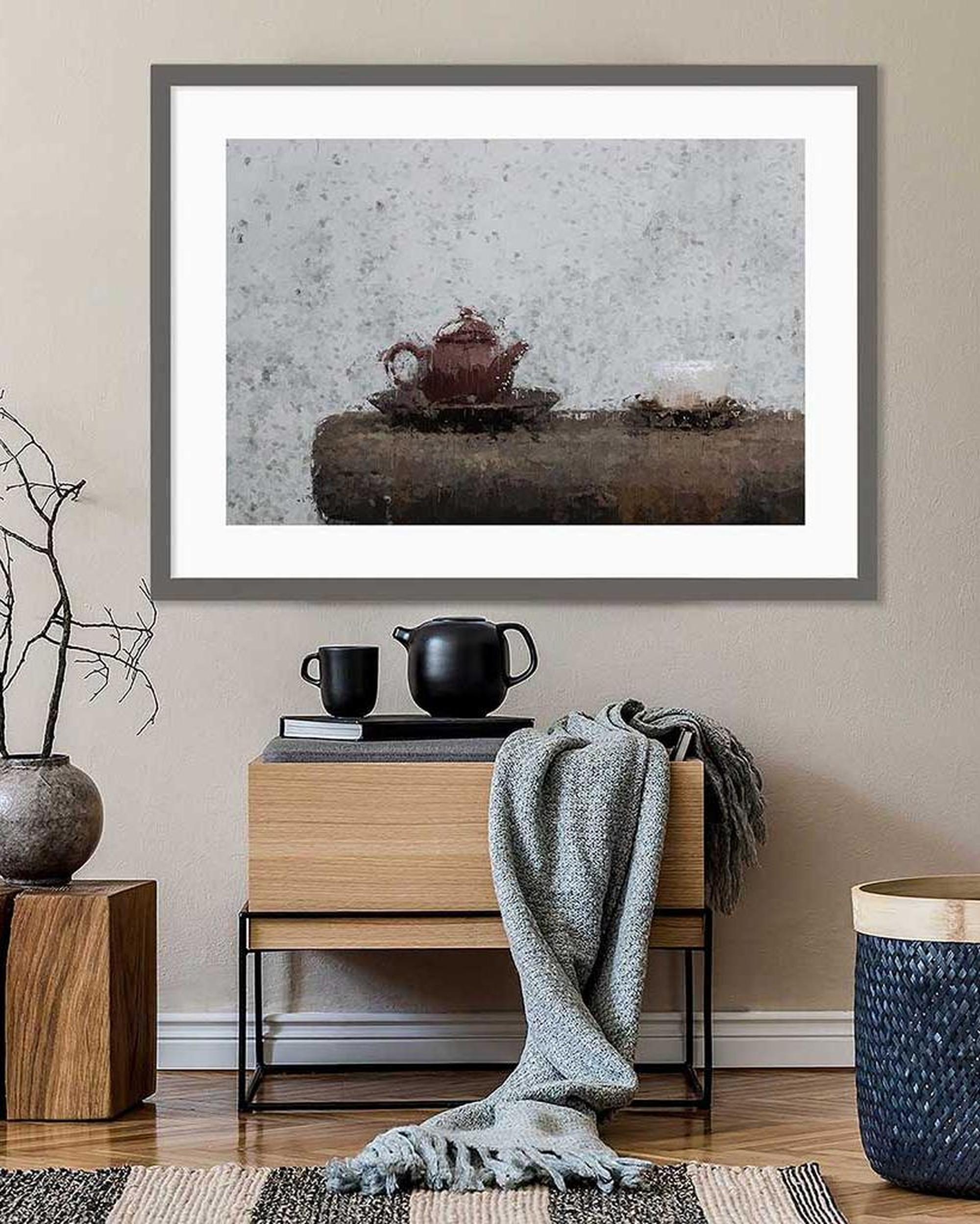 Framed artwork of a teapot on a table with a wooden cabinet and decorative items in a room.