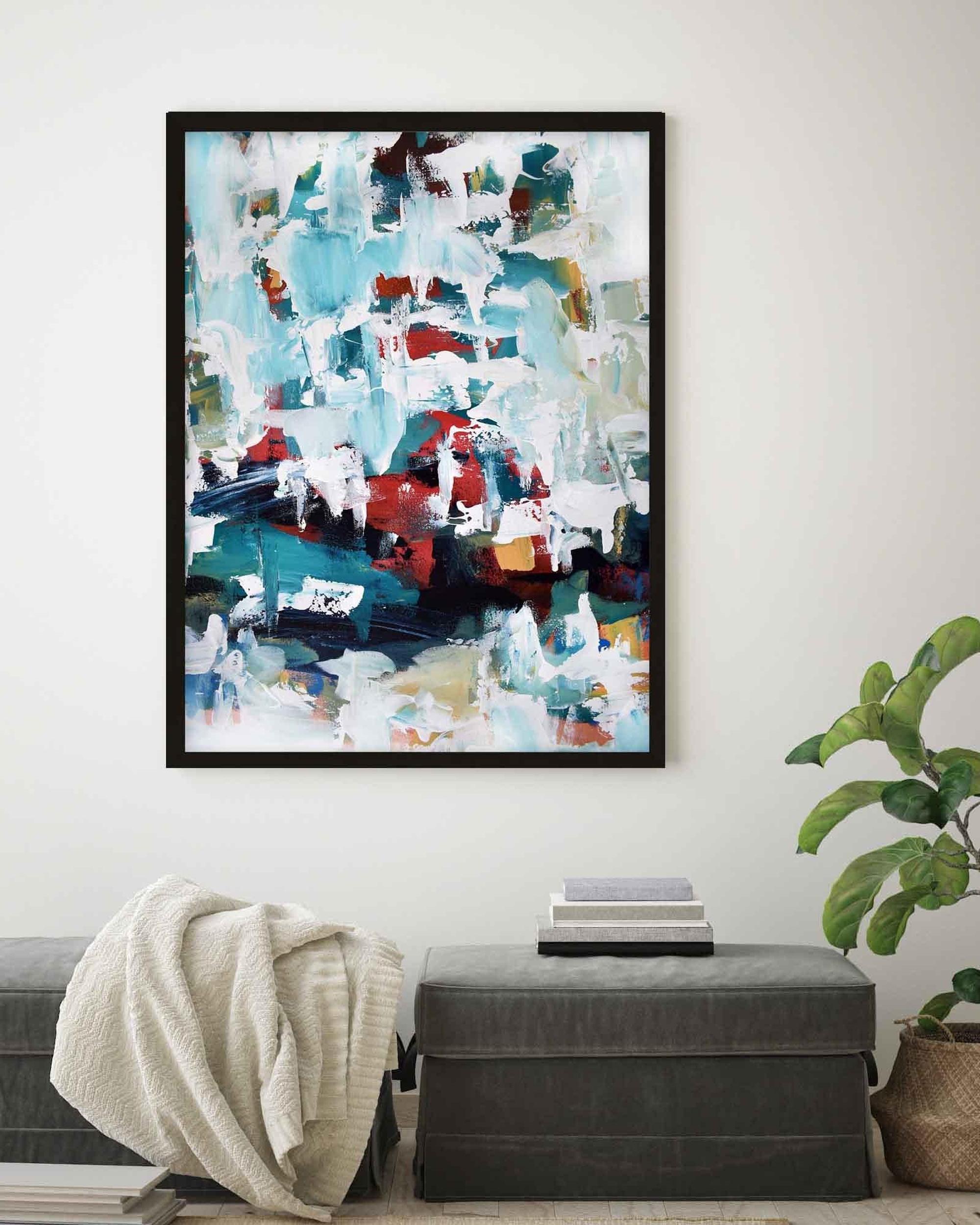 Abstract art print in a black frame on a wall above a bench with a plant.