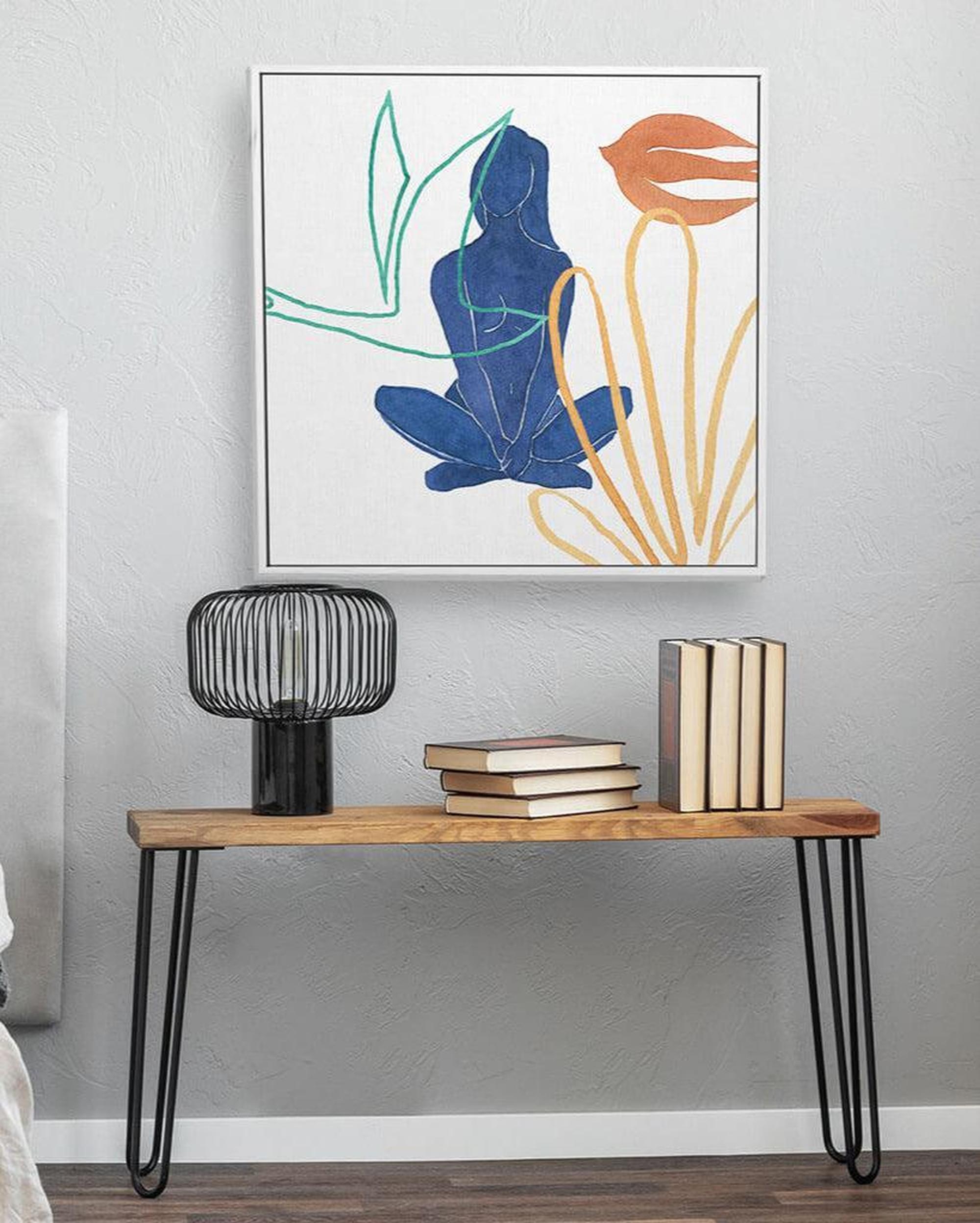 Modern interior with a wooden console table, books, and a decorative lamp against a gray wall with abstract art.