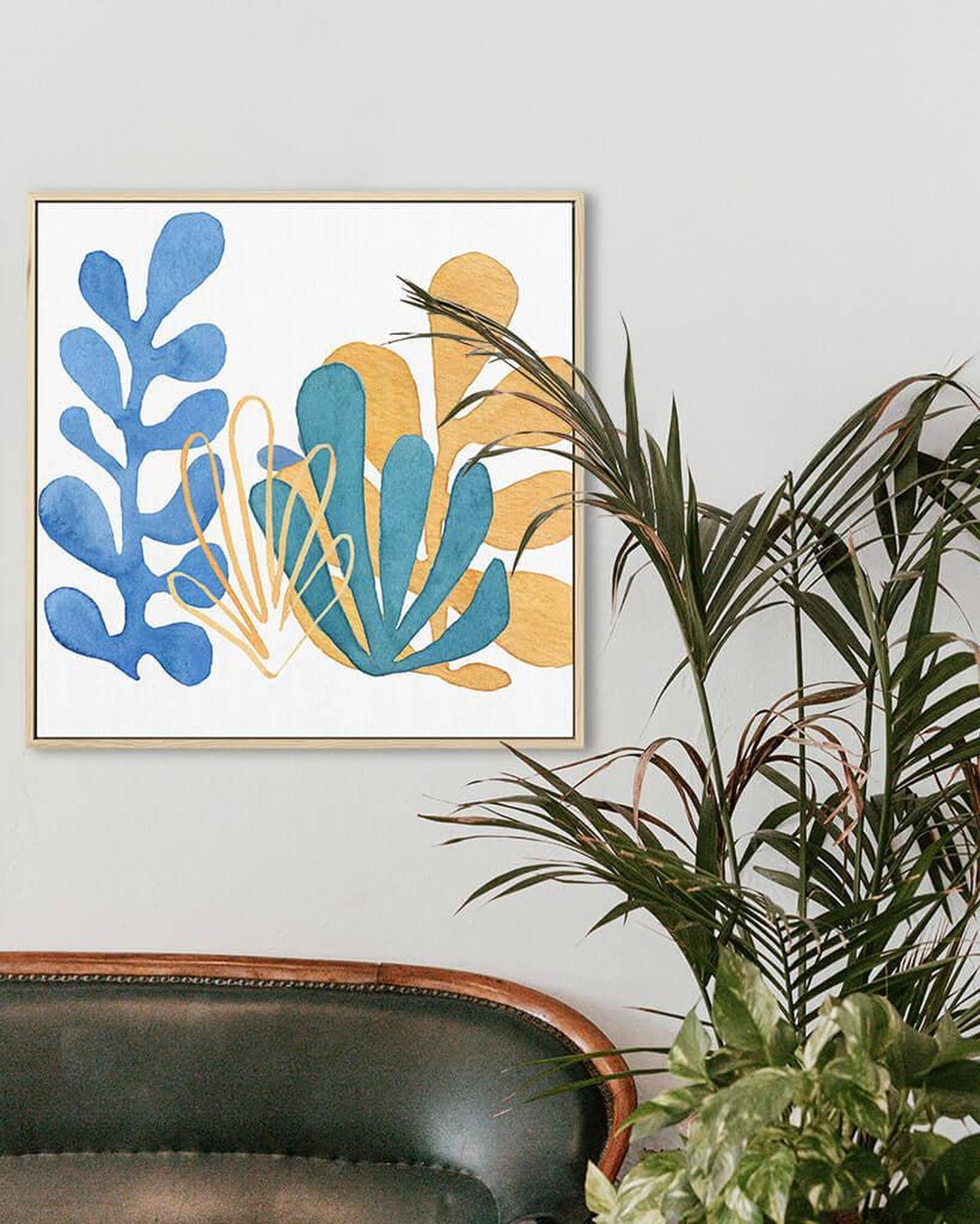 A canvas print featuring an abstract design with blue, yellow, and brown colors, framed and hanging on a wall above a plant.