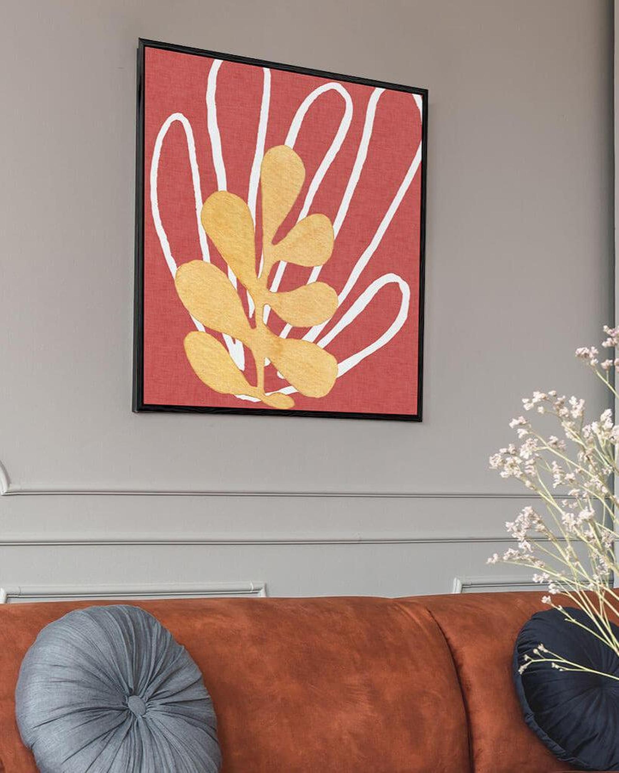 A framed canvas print featuring a red and yellow abstract pattern, displayed on a wall above a brown sofa, with a decorative vase and cushions in the foreground.