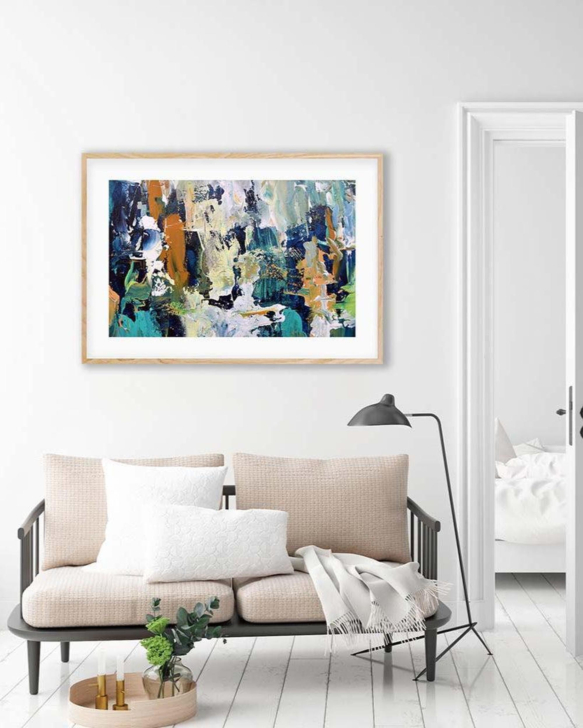 Abstract painting in a wooden frame on a white wall above a beige sofa.