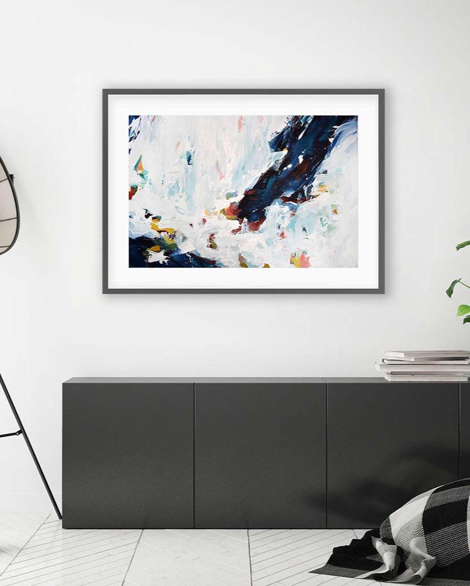 Framed abstract art piece on a white wall above a black cabinet.