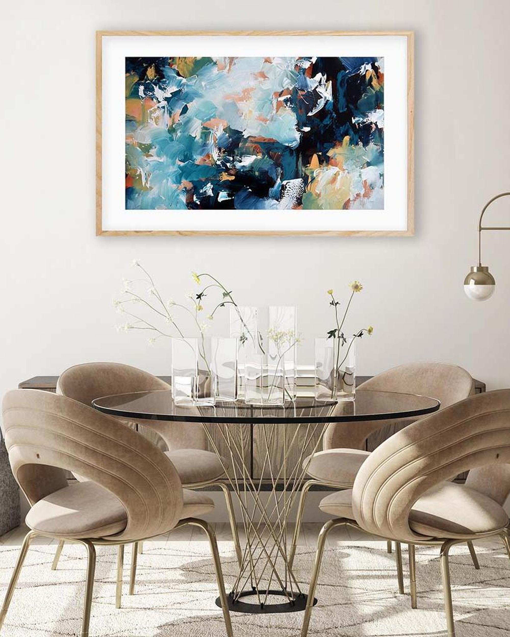 Dining room with a round glass table and beige chairs, featuring abstract art on the wall.