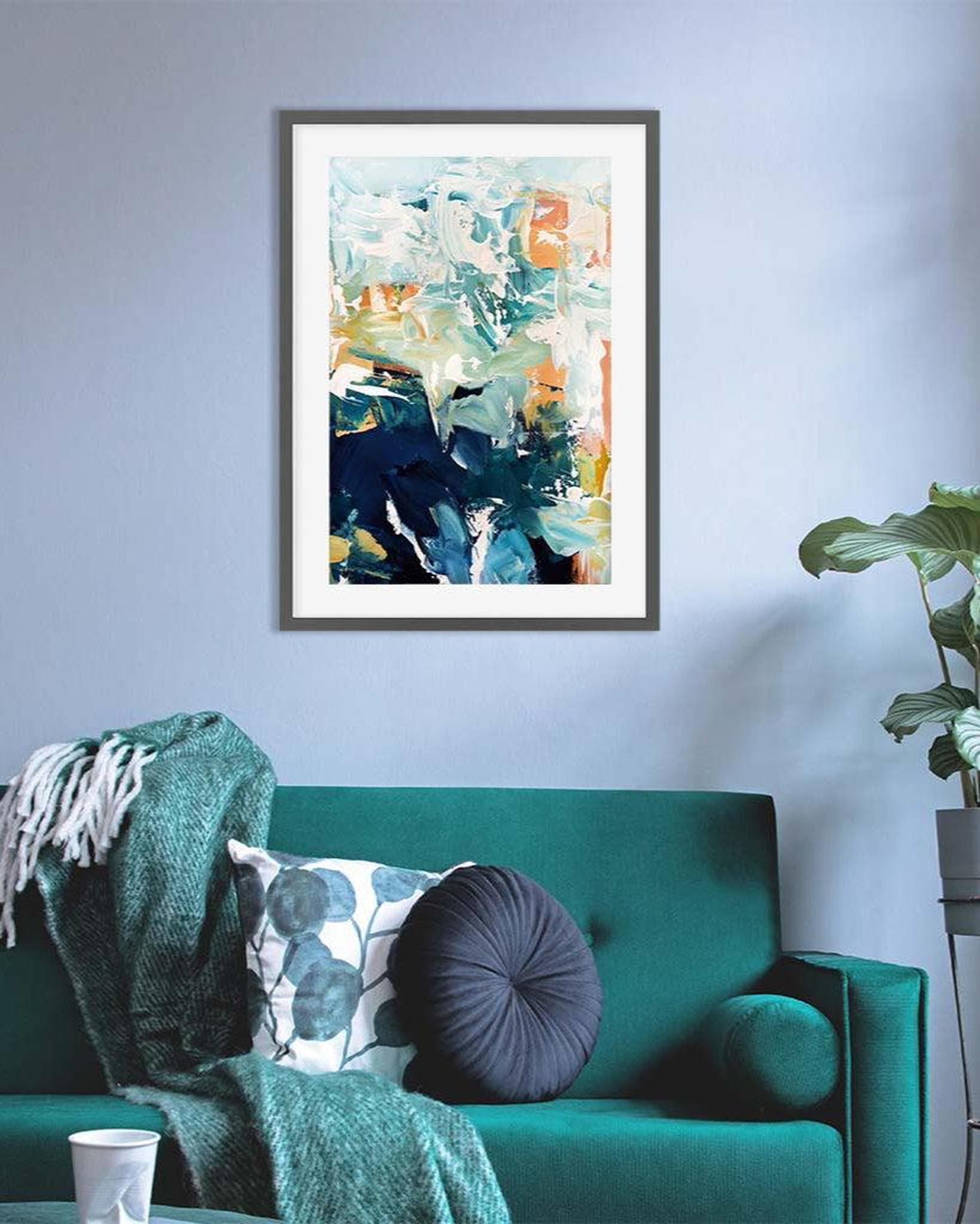Framed abstract art above a green sofa with decorative pillows and a plant.