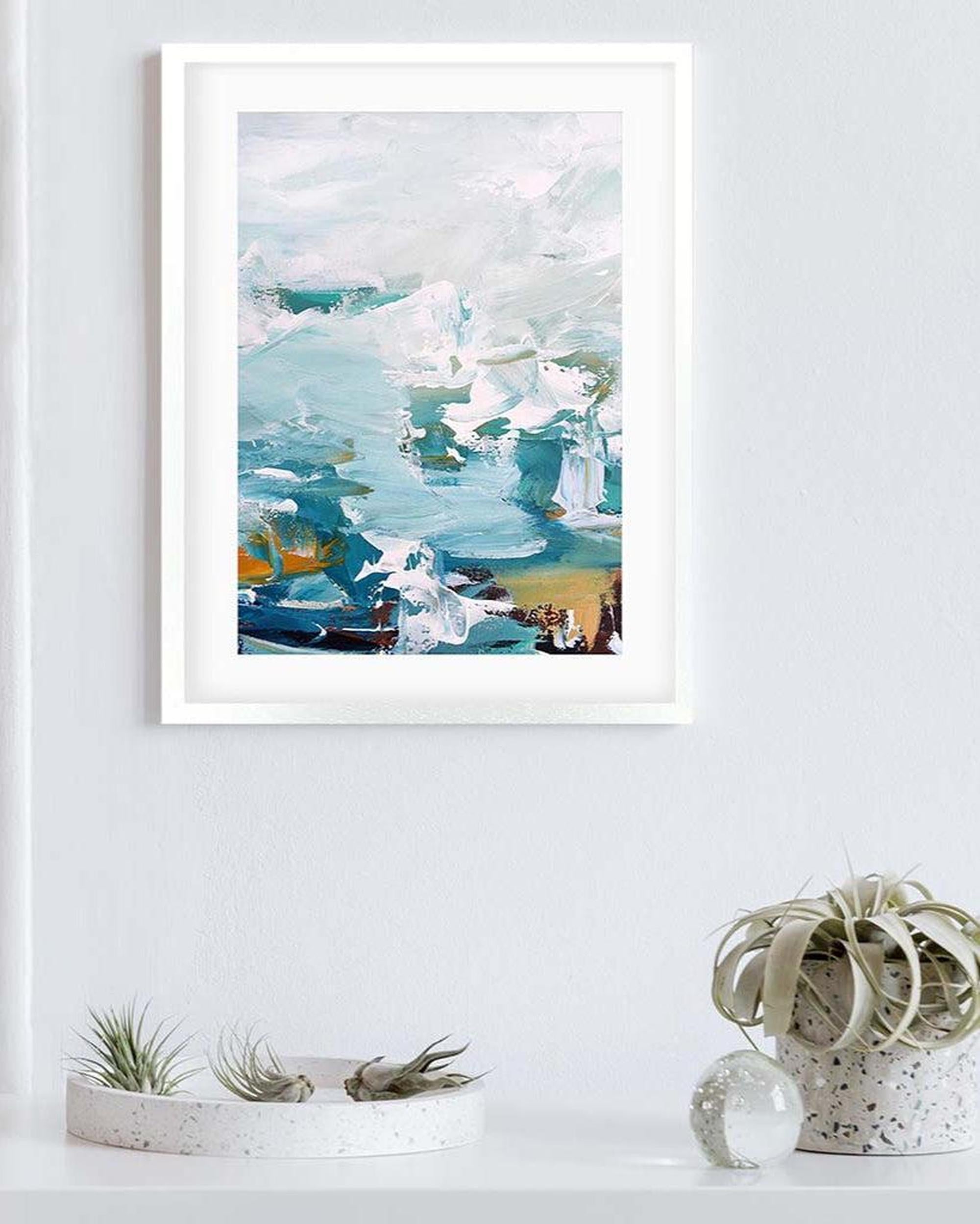 Framed abstract artwork on a white wall with decorative plants below.