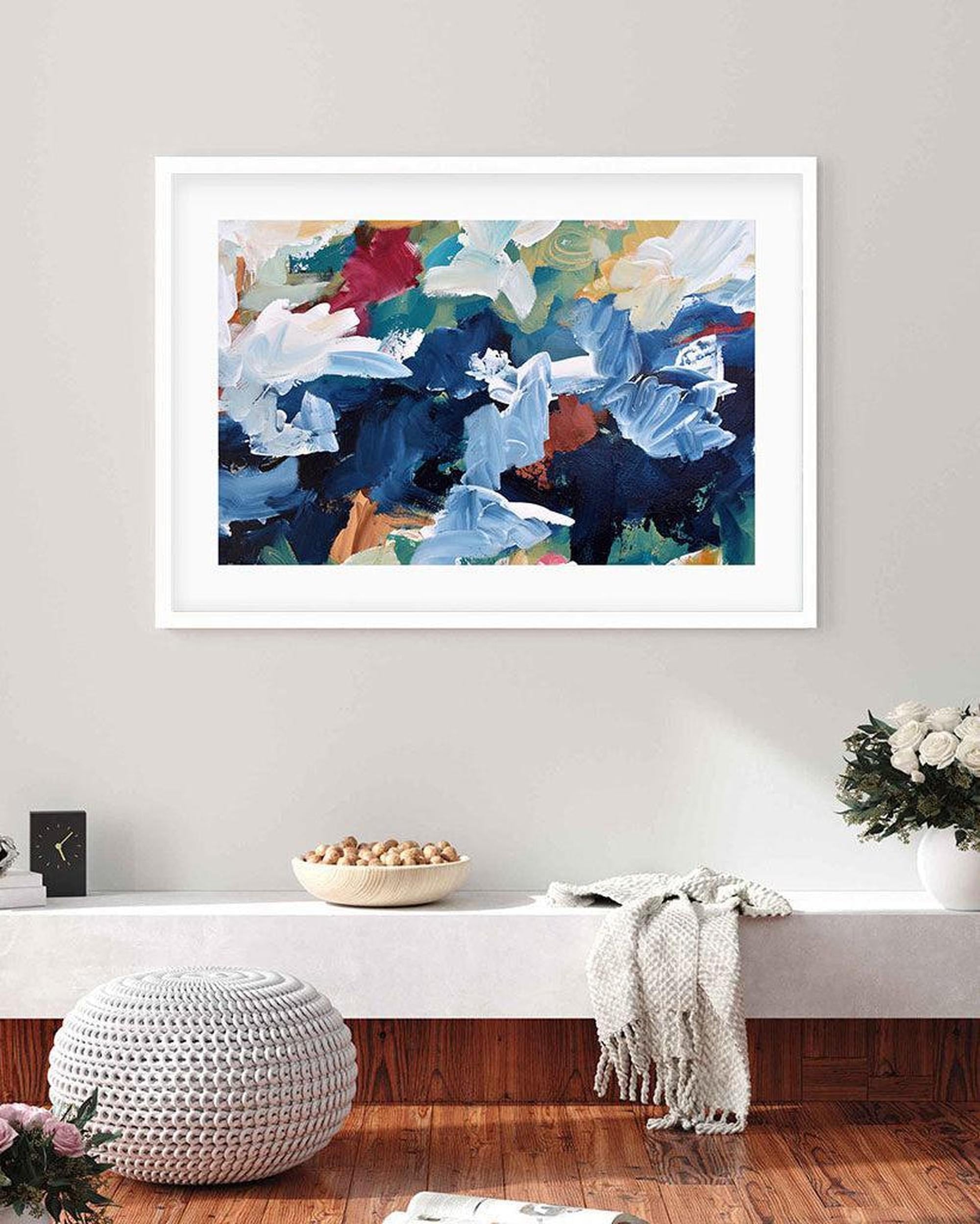 Framed abstract artwork with blue and white flowers on a wall above a white console table.