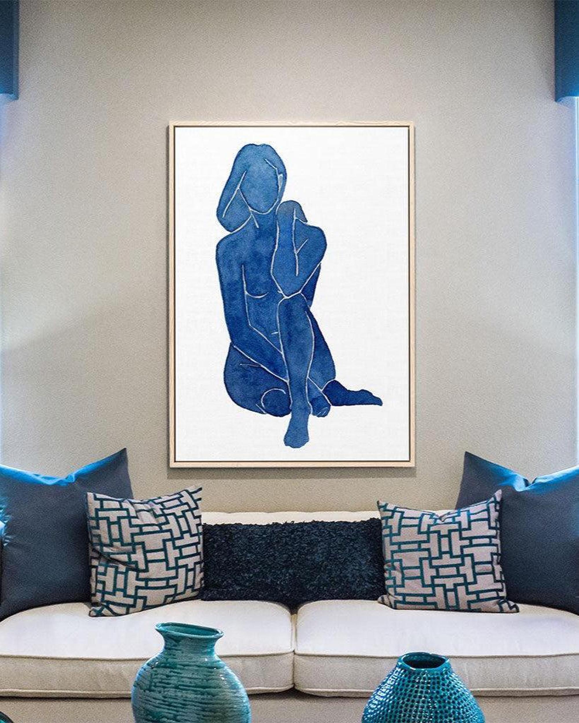 Framed abstract art of a blue figure on a wall above a beige sofa with decorative pillows.