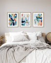 Three abstract art prints above a bed in a bedroom setting.