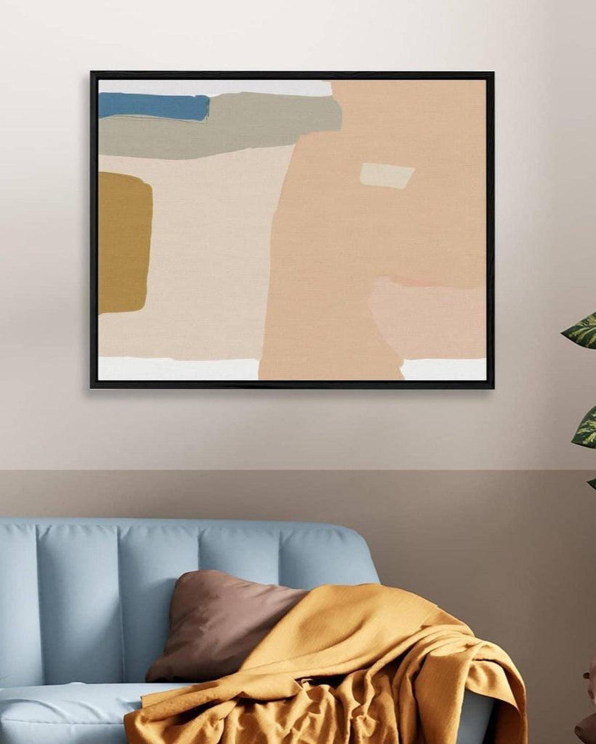 Abstract art print in a black frame on a wall above a blue sofa with a yellow blanket.