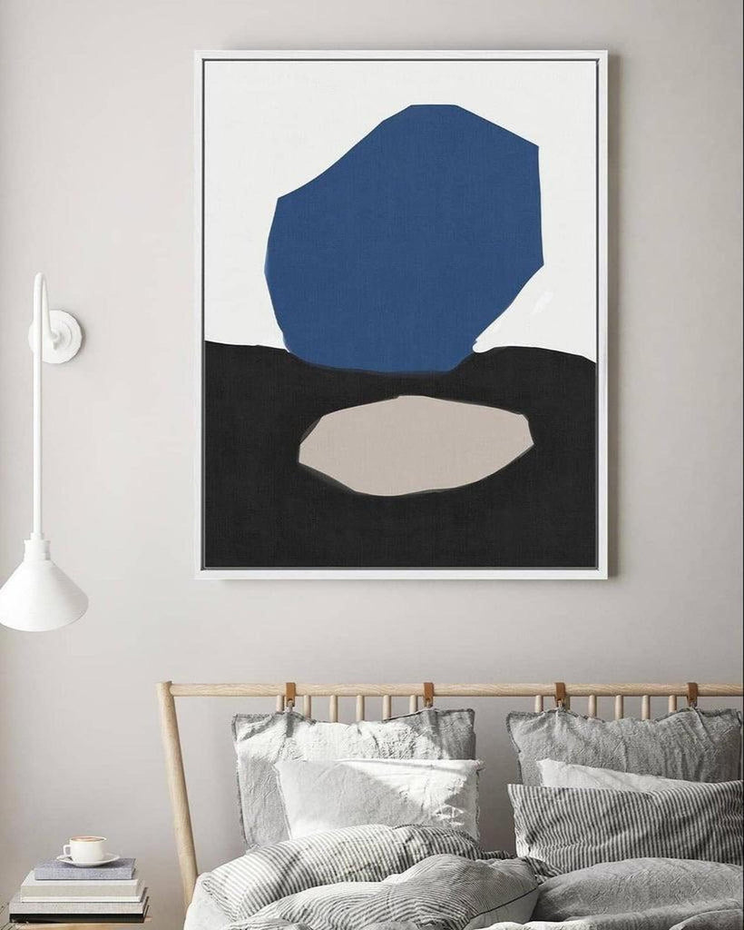 Abstract art print with blue, black, and beige shapes on a wall above a bed.