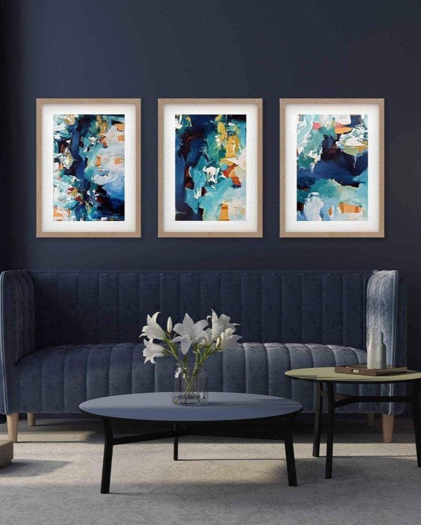 A set of three framed abstract art prints displayed above a dark-colored sofa in a living room setting.
