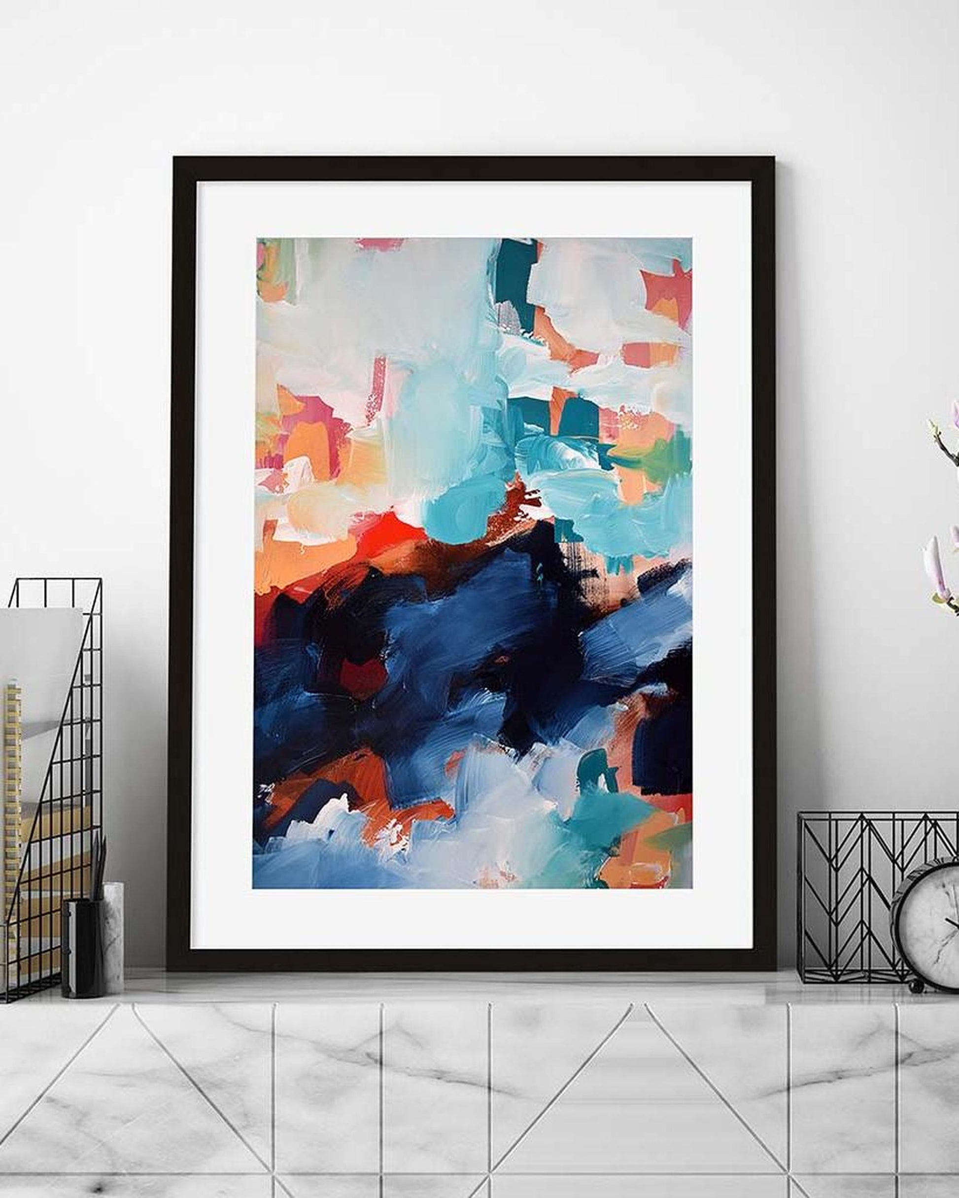 Framed abstract art print with colorful brush strokes on a white wall.