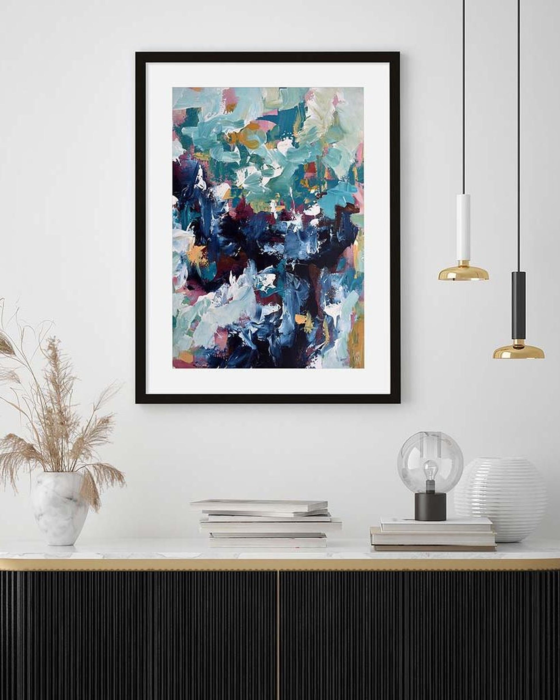Framed abstract art print on a wall above a wooden shelf with decorative items.