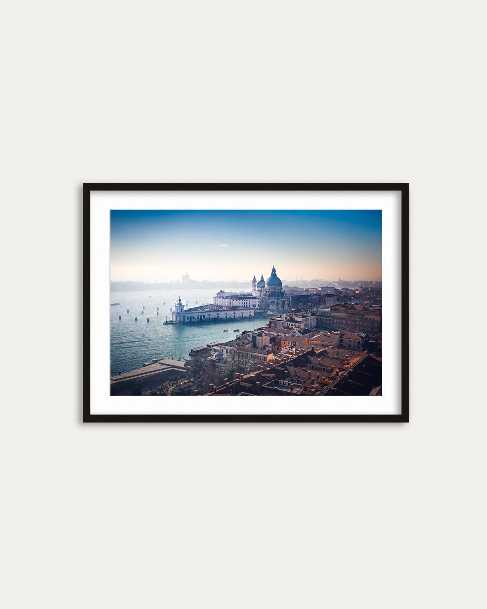 Framed photograph of a cityscape with a large building and water body on a white wall.