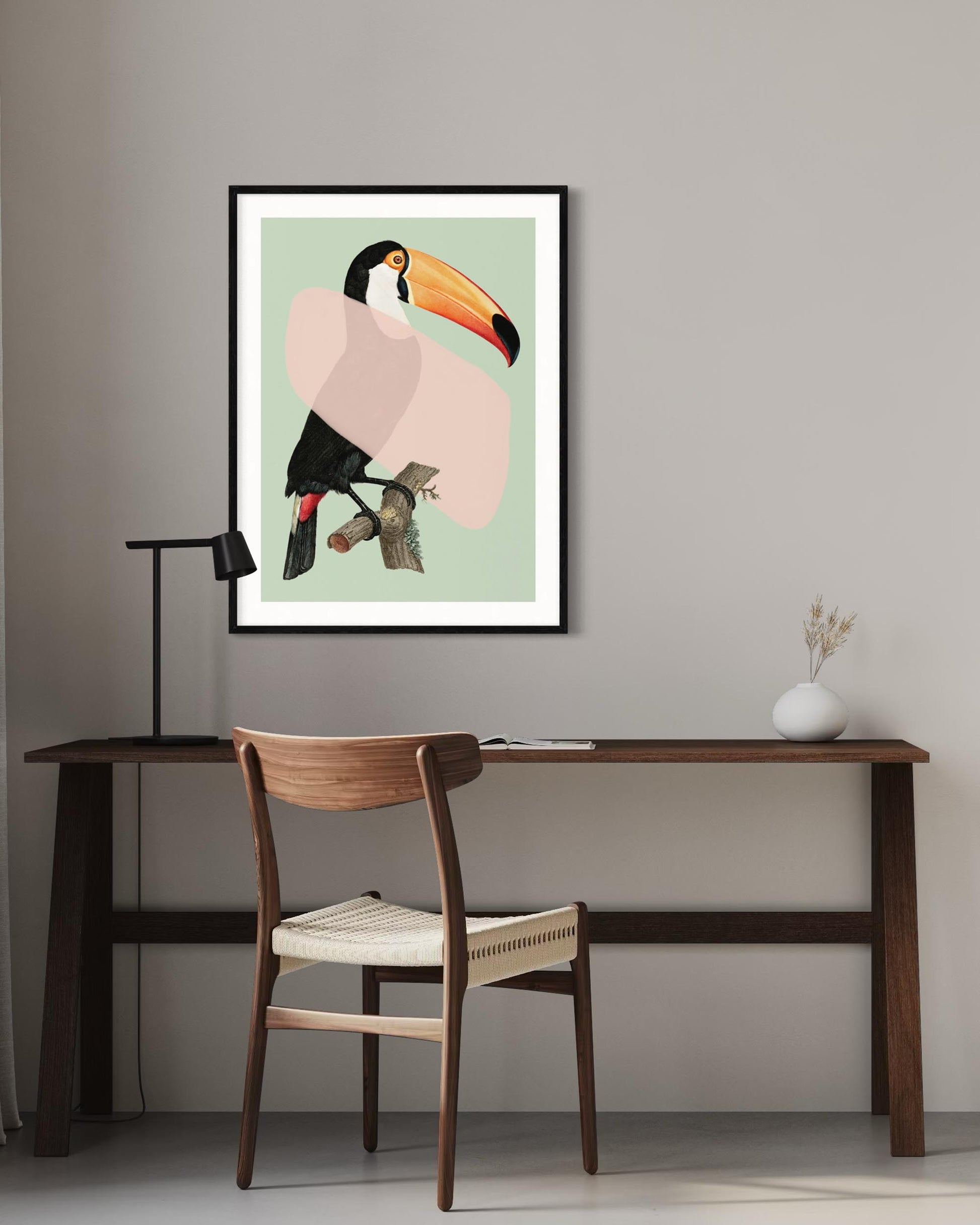 Framed artwork of a toucan on a wall above a desk with a chair.