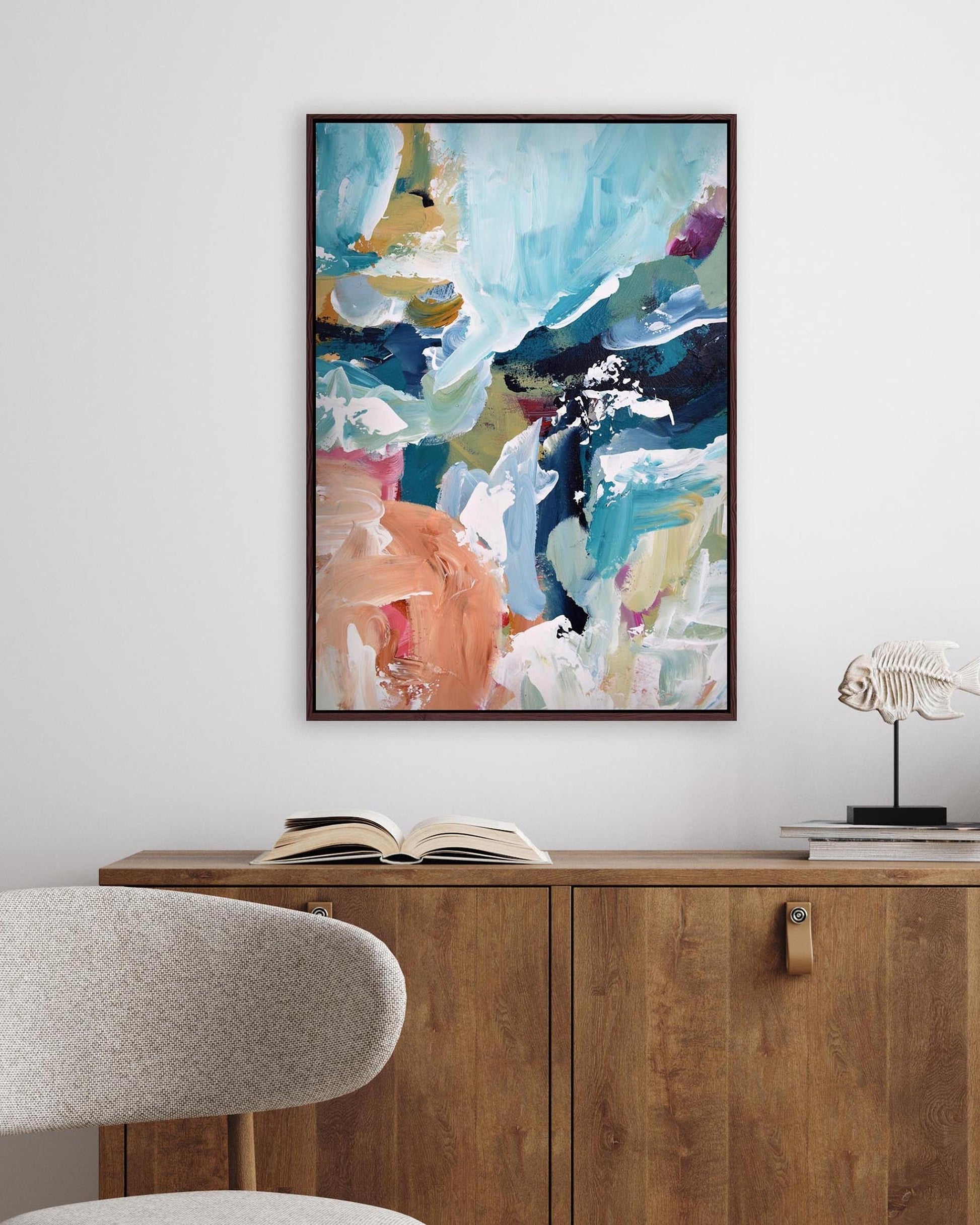 Abstract painting on a wall above a wooden cabinet with an open book and decorative items.