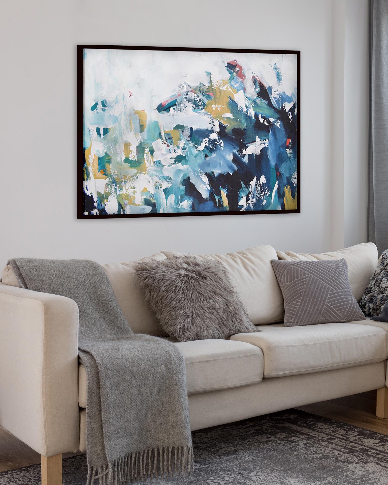 Beige sectional sofa with decorative pillows and a gray throw blanket, featuring a colorful abstract painting on the wall.