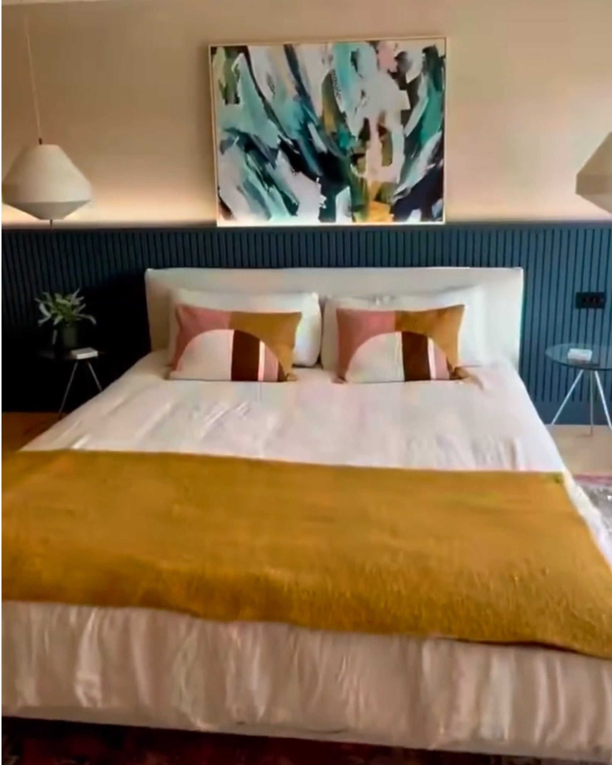Bedroom with a bed featuring yellow blanket and colorful pillows, abstract painting on the wall.