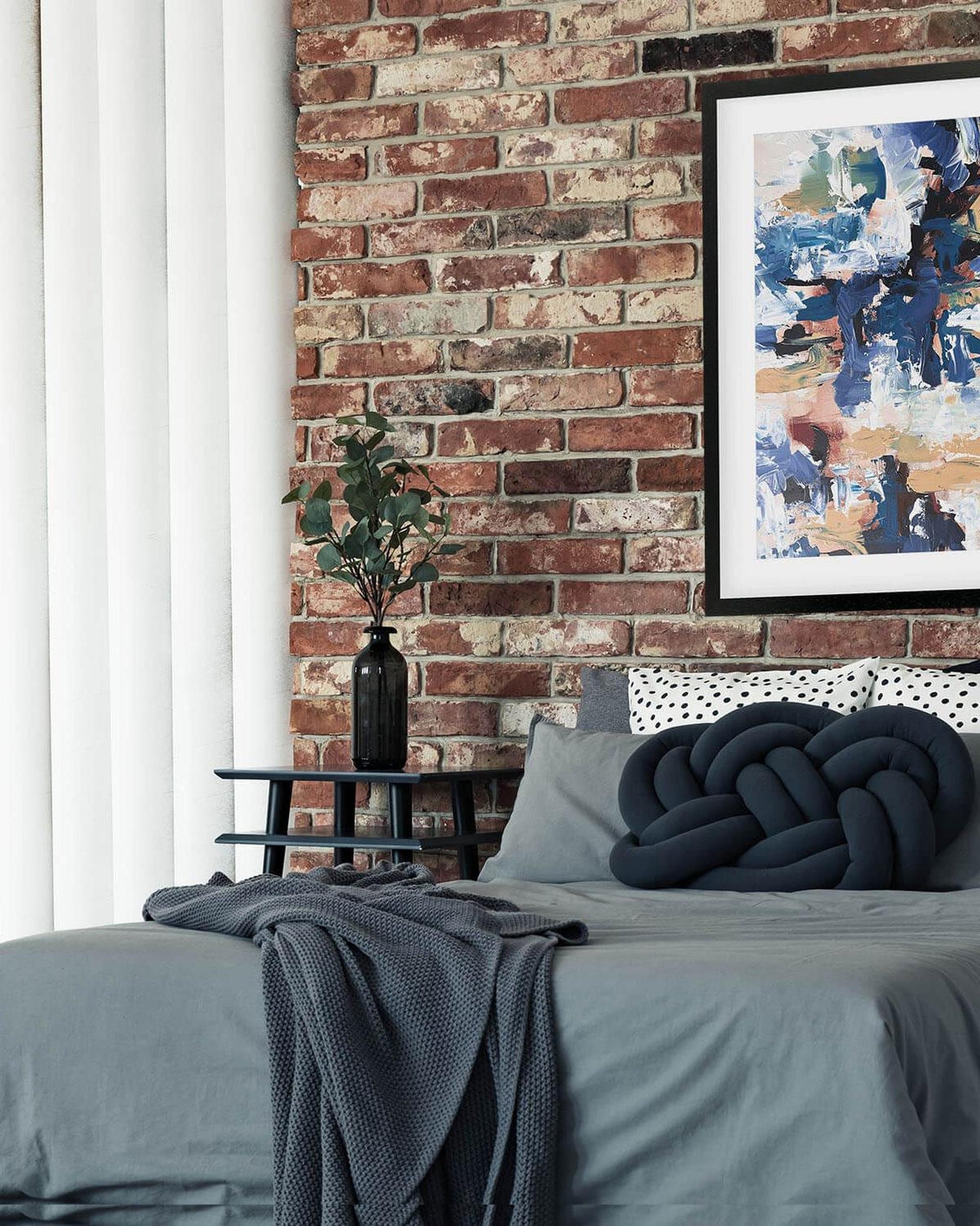 Bedroom with brick wall, abstract art, and decorative pillows