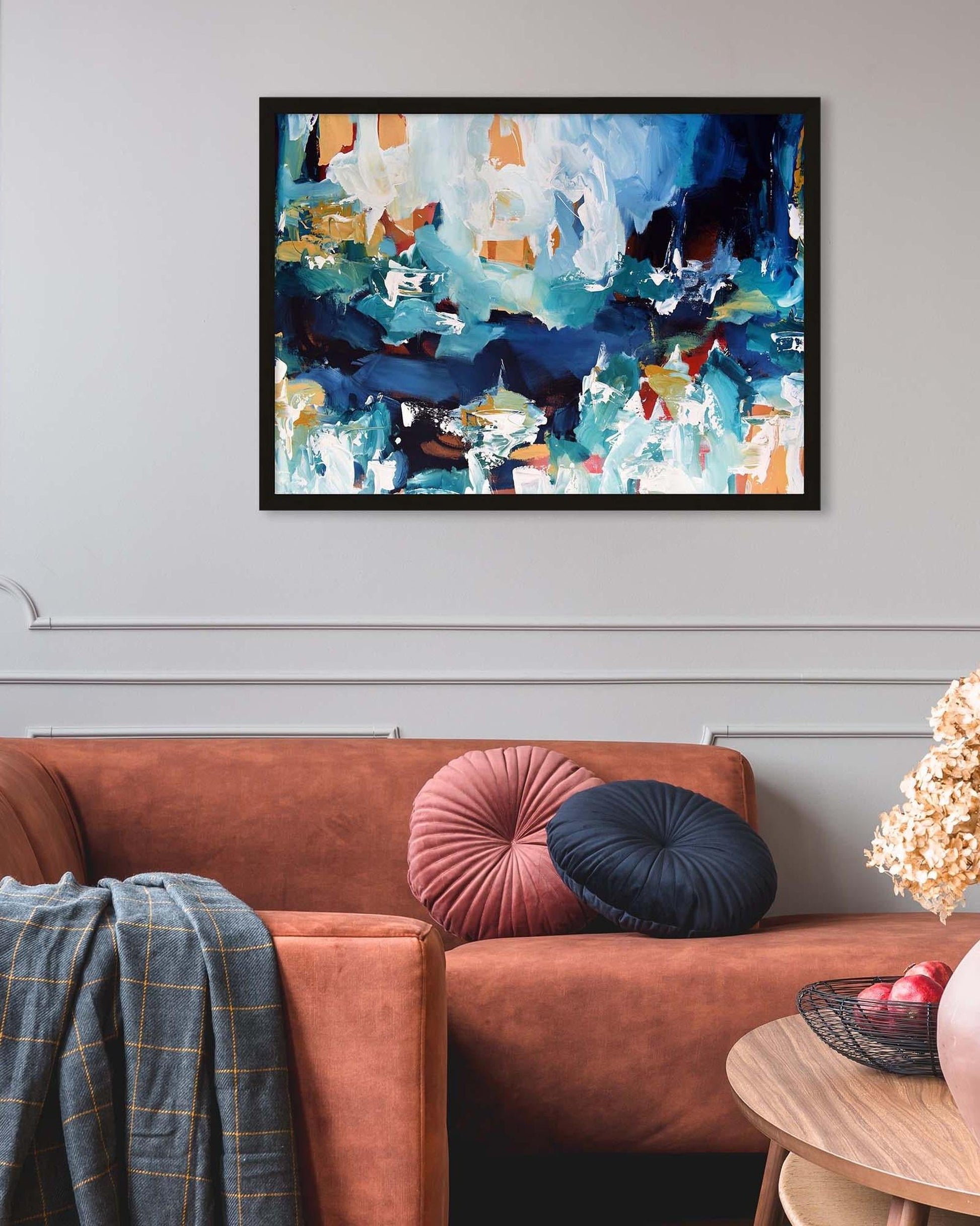 Abstract painting on a wall above a brown sofa with colorful cushions.