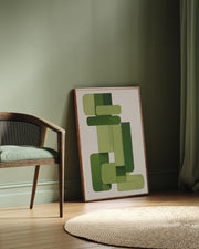 Framed abstract art with green shapes leaning against a wall next to a chair.