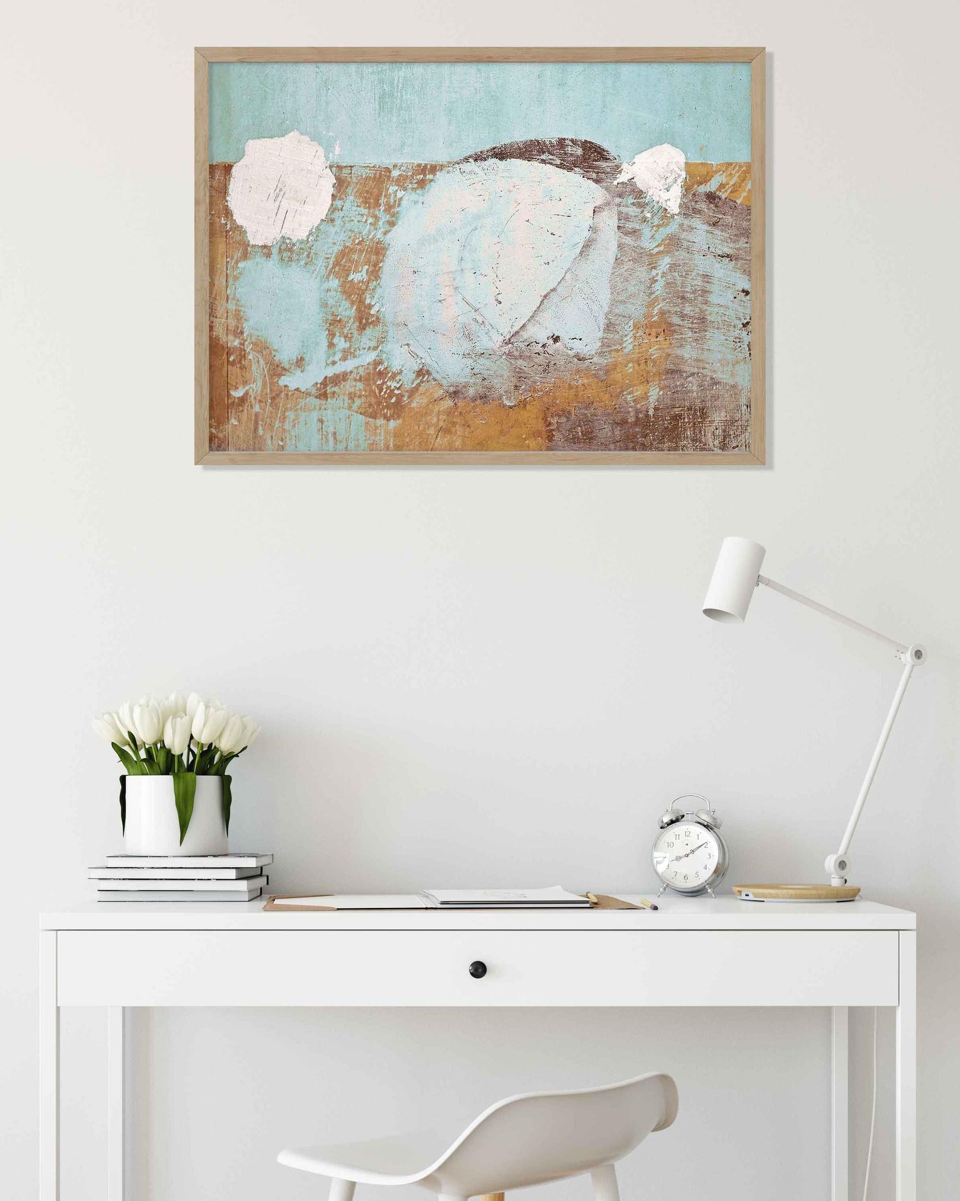 Abstract painting on a wall above a white desk with a lamp and decor items.