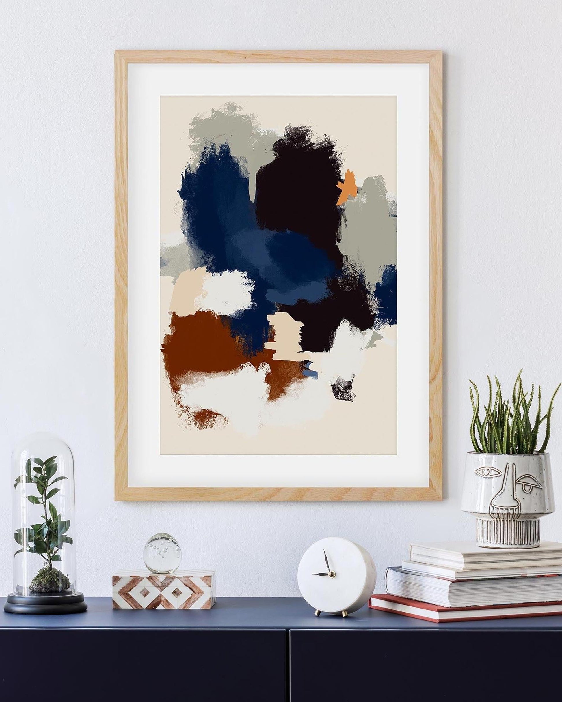 Framed abstract art piece on a wall with decorative items below.