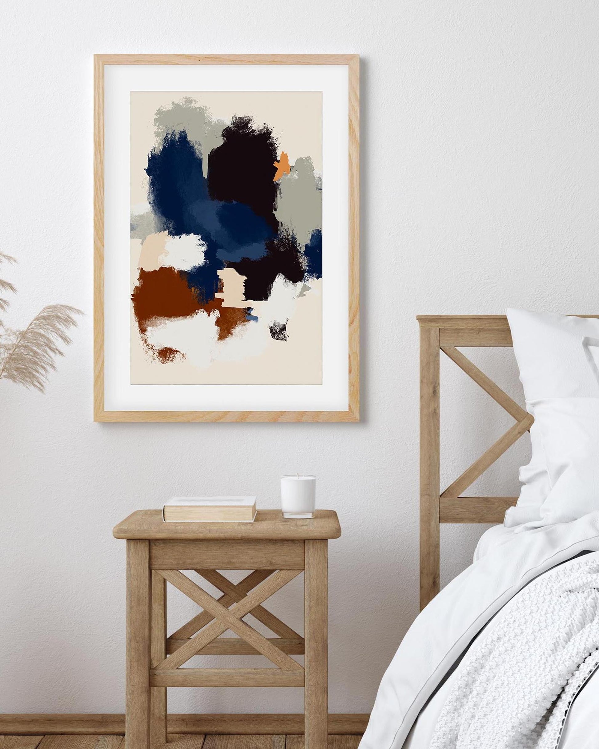 Abstract art print in a wooden frame on a wall above a wooden side table in a bedroom.