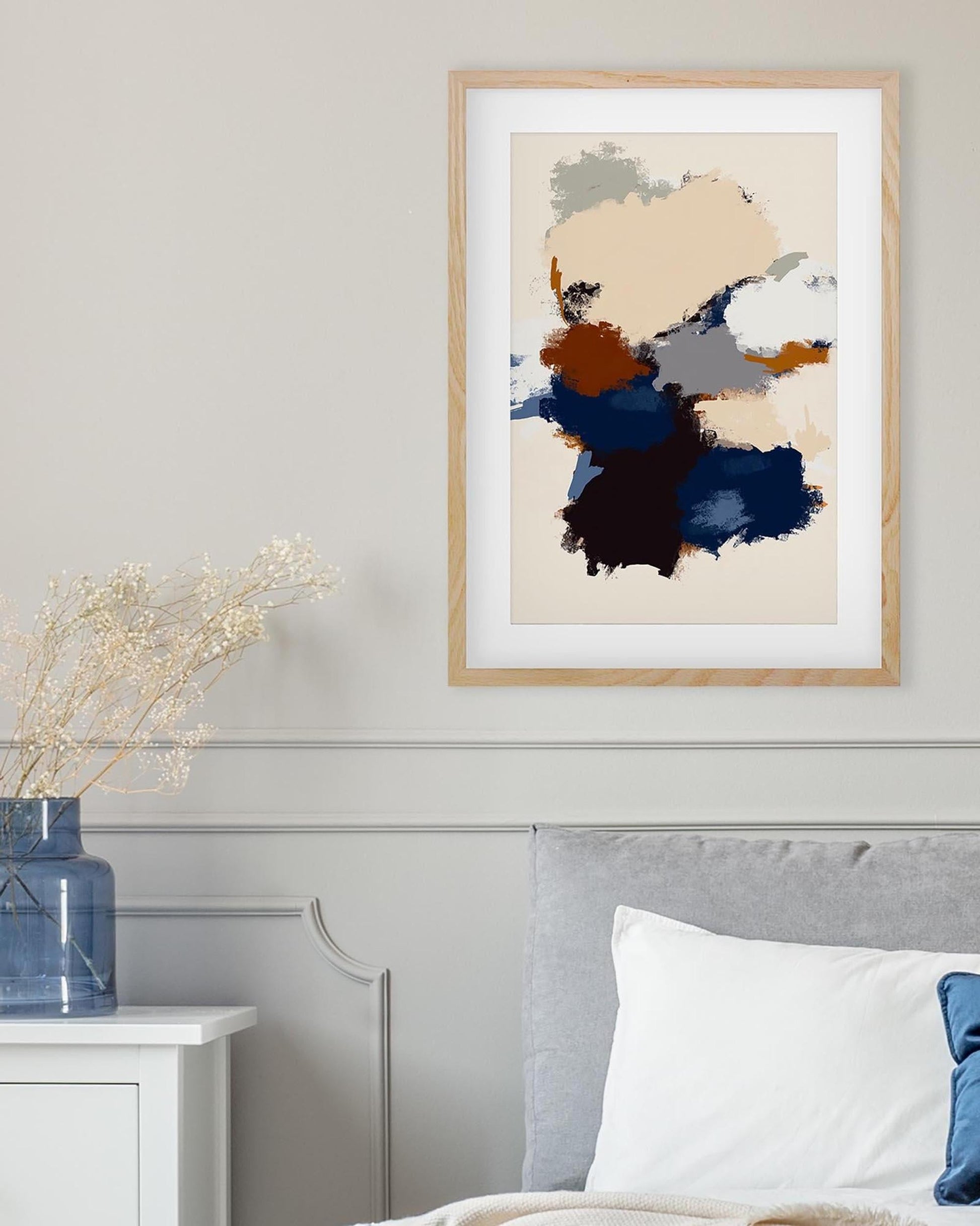 Abstract art print in a wooden frame on a wall above a bed