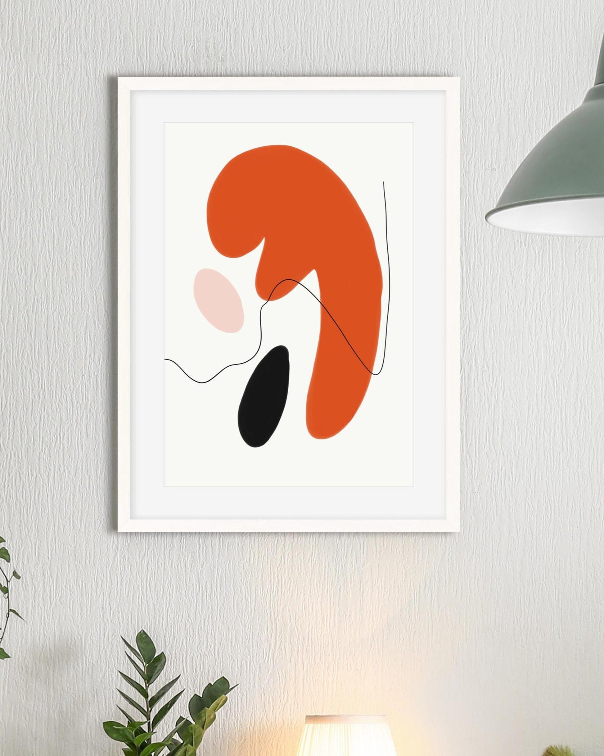 Framed abstract art print with orange, pink, and black shapes on a light gray wall.