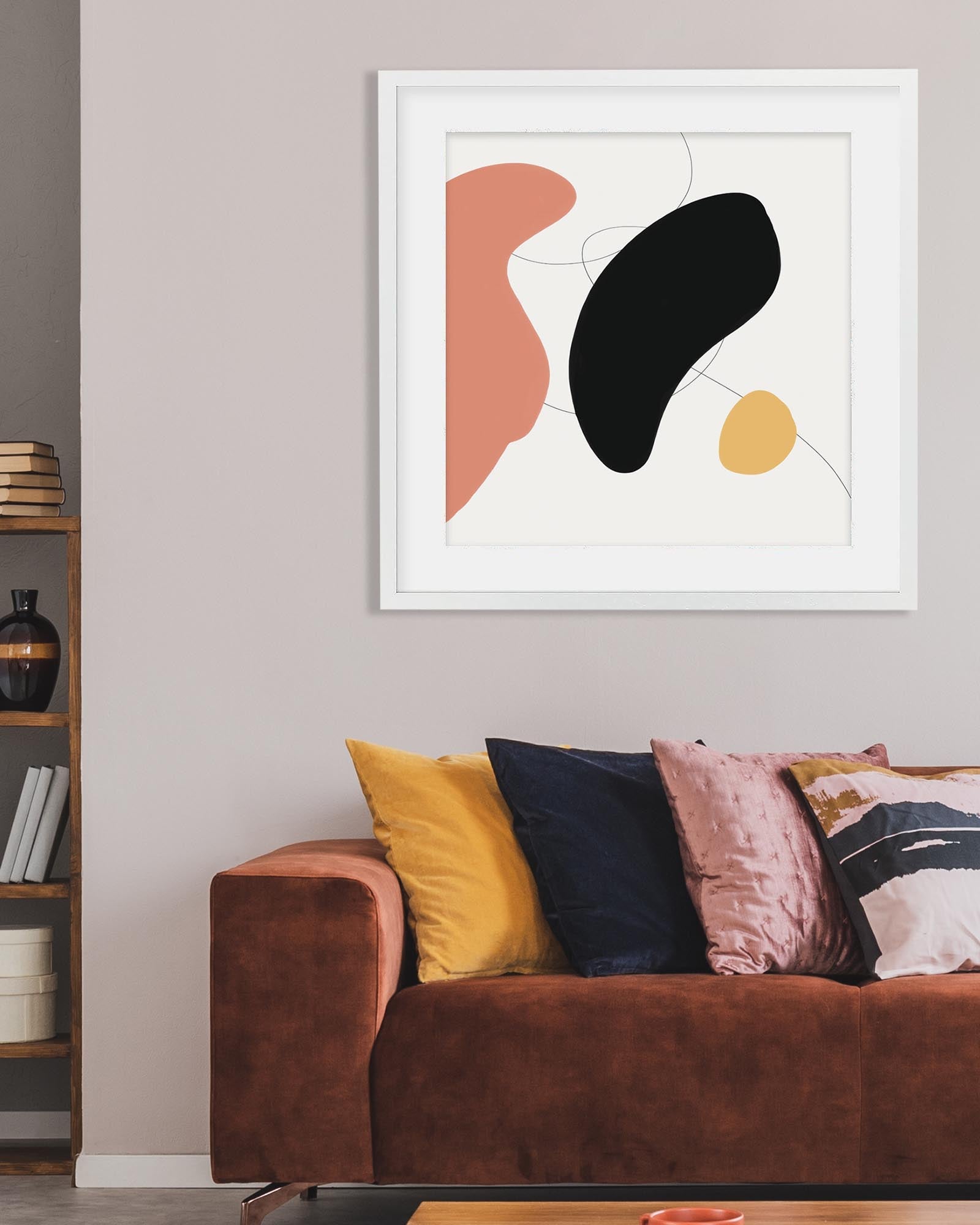 Abstract art print on a wall above a brown sofa with colorful cushions.