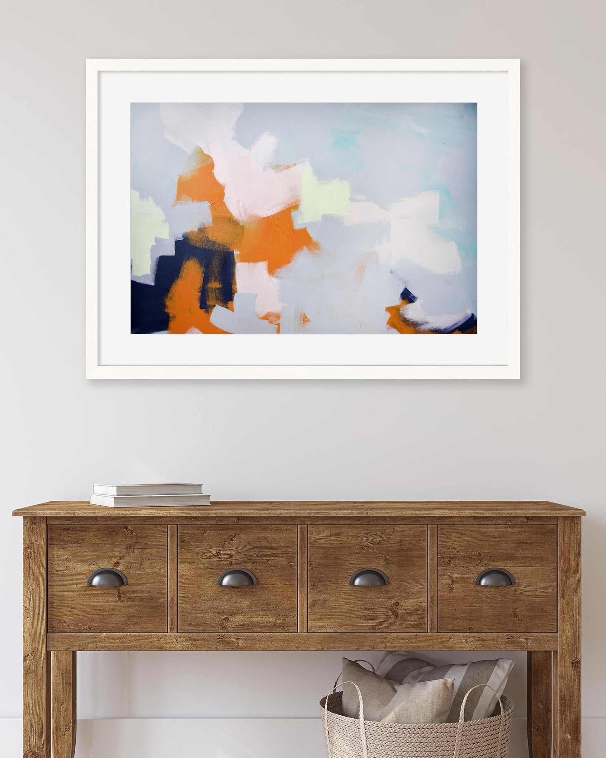 Framed abstract art above a wooden console table with a basket and books.