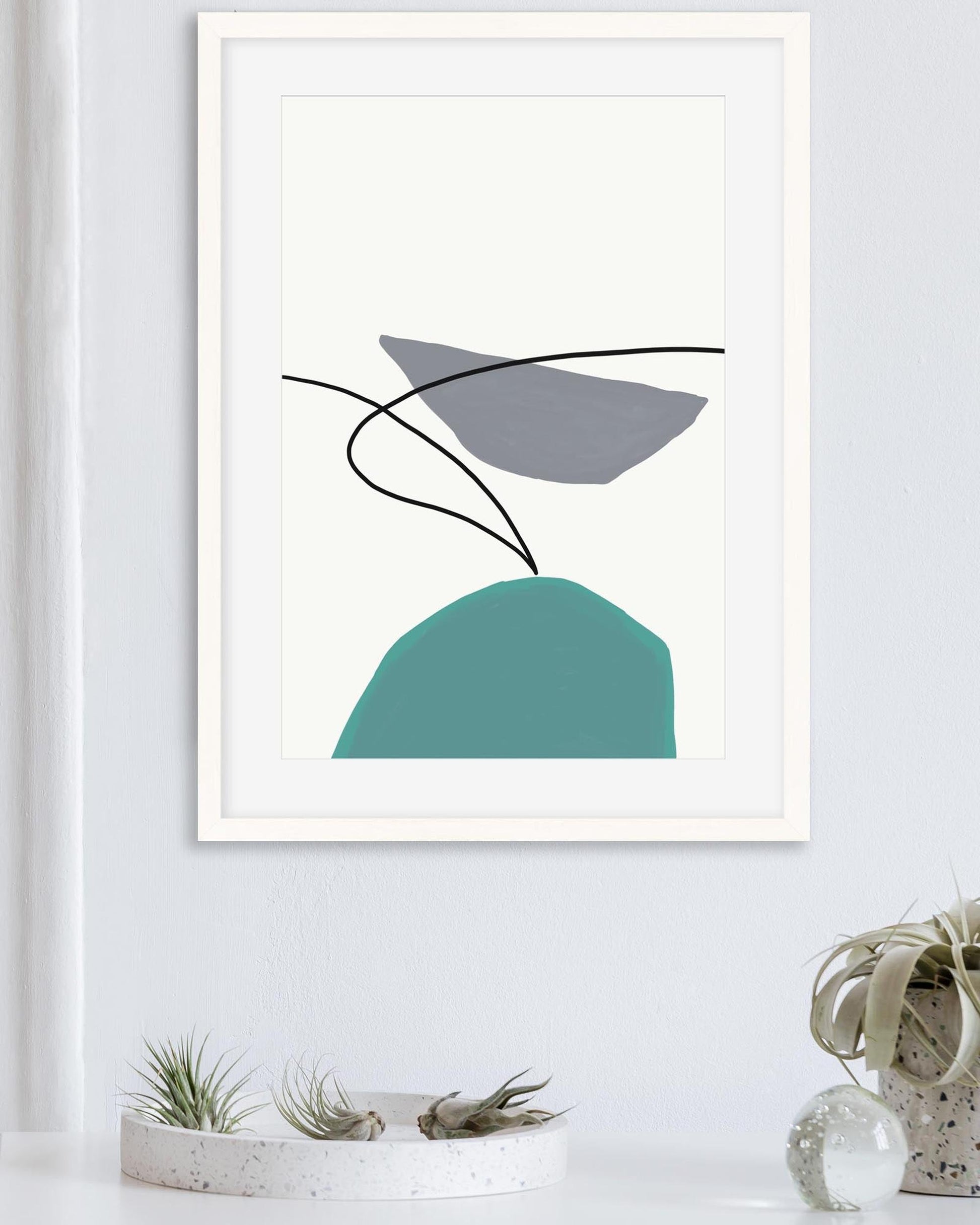 Framed abstract art print with geometric shapes on a white wall.