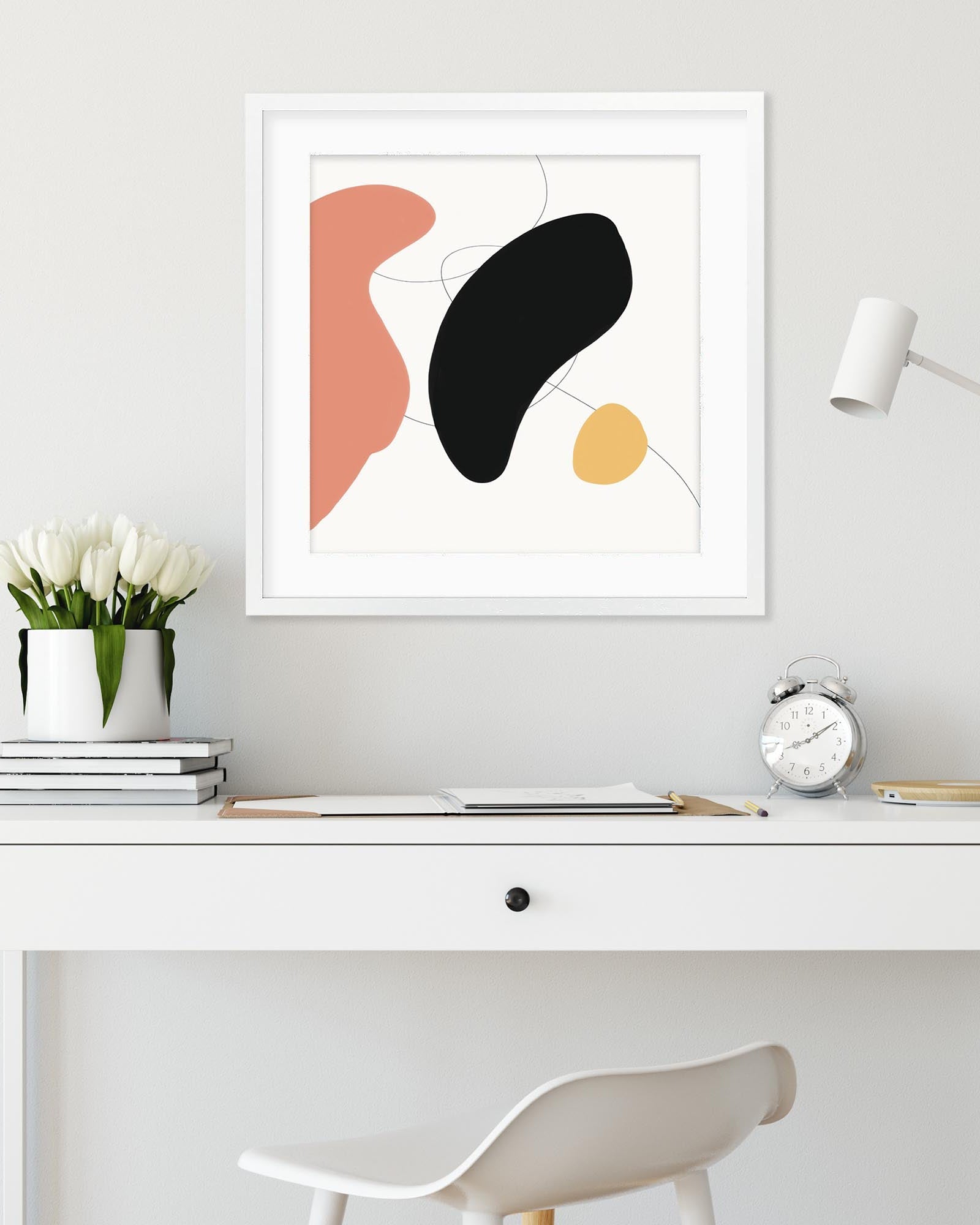 Abstract art print on a wall above a desk with a lamp and clock.