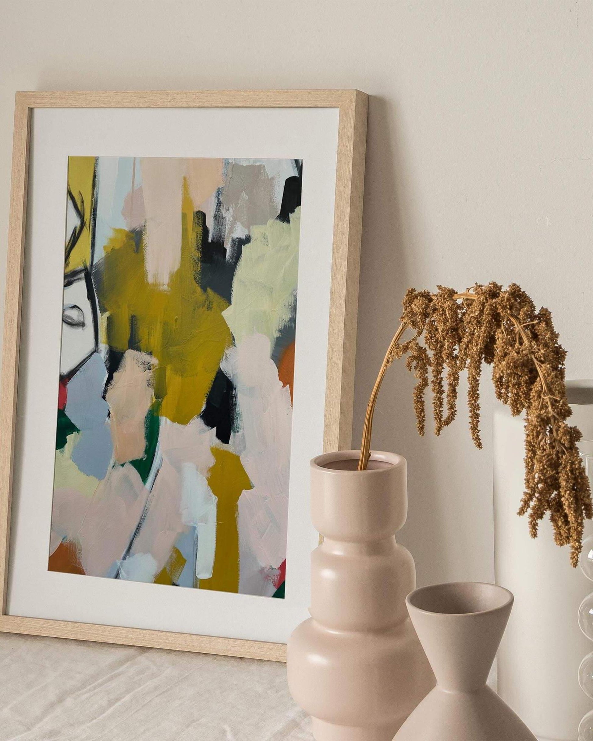 Framed abstract art piece on a wall with decorative vases below.