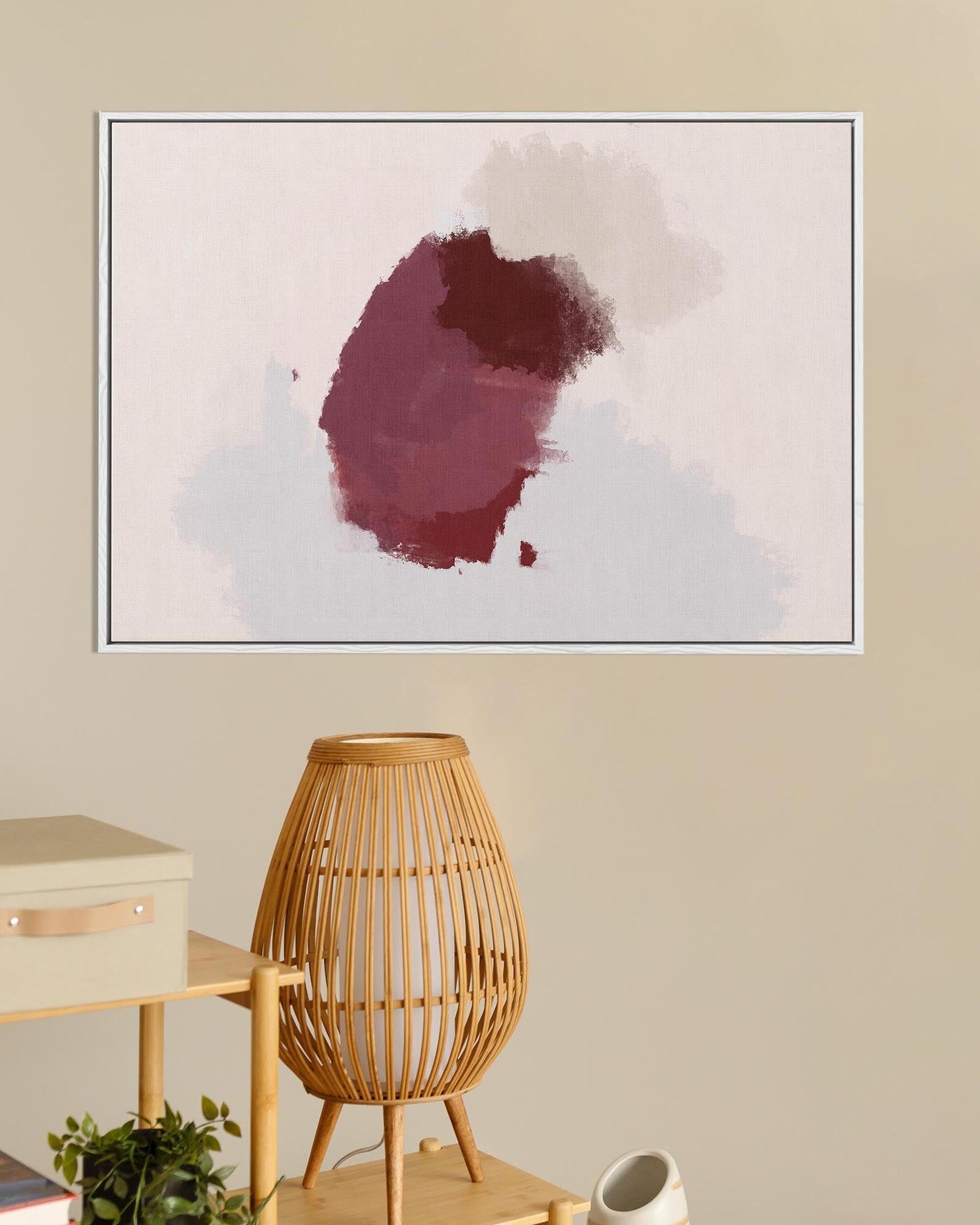 Framed abstract art piece with a red and white design on a beige wall, below a wooden lamp and side table.