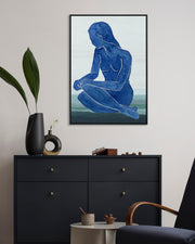 Framed abstract art of a blue figure on a wall above a black dresser.