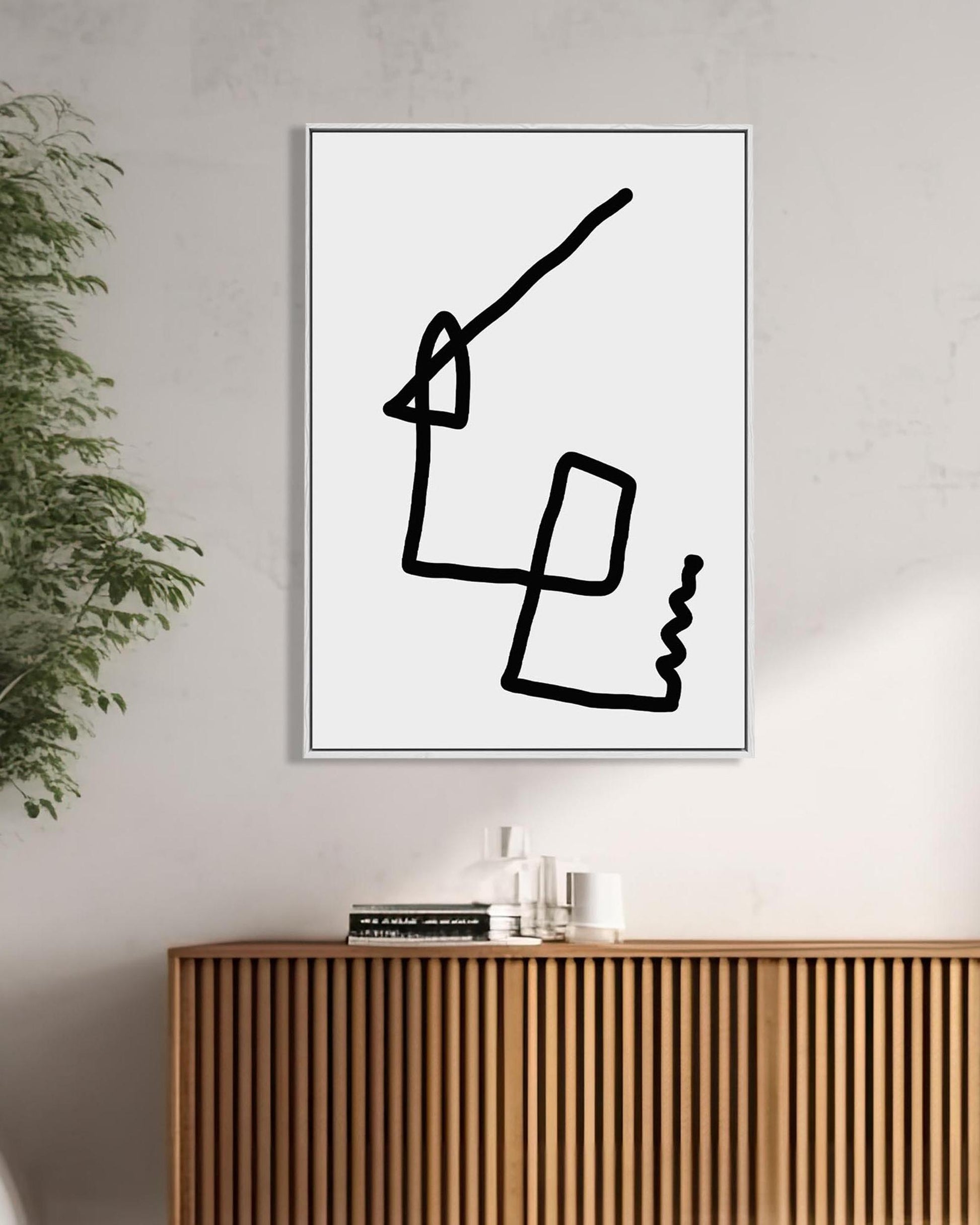 Modern abstract art print on a wall above a wooden cabinet with a plant to the left.