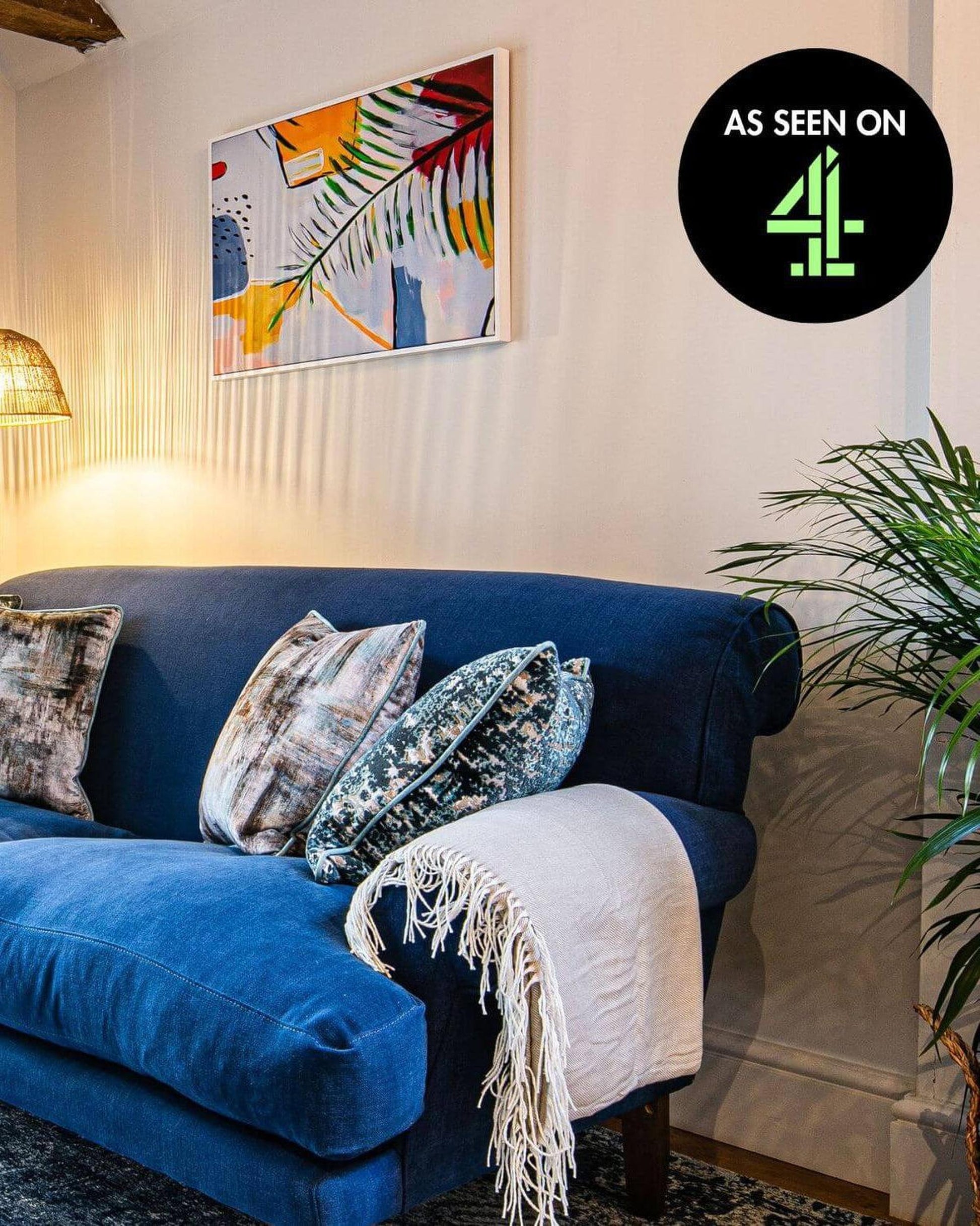 Blue sofa with decorative pillows and a blanket in a living room setting, featuring a 'As Seen on 4o' logo.