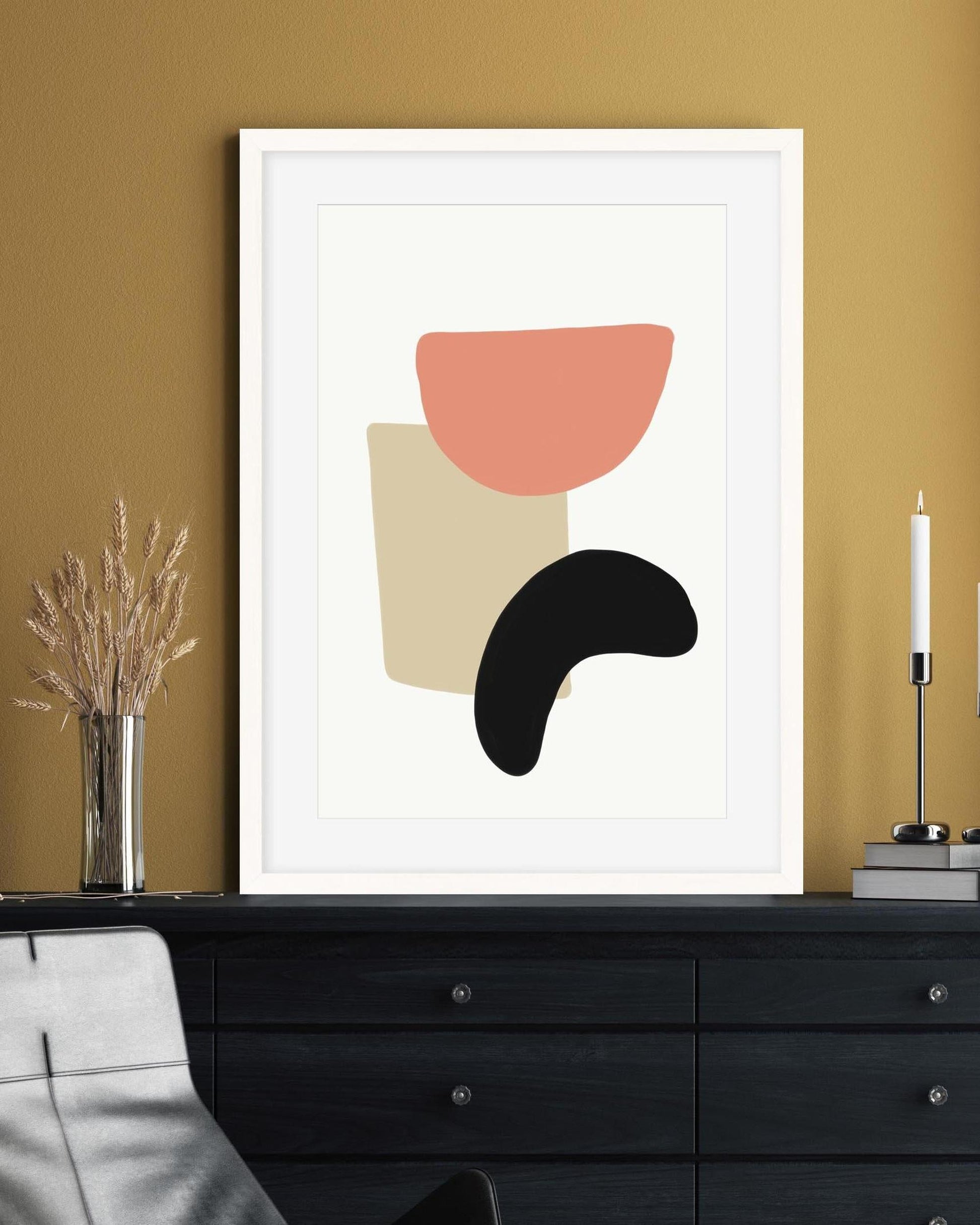 Framed abstract art print with geometric shapes on a wall above a black dresser.