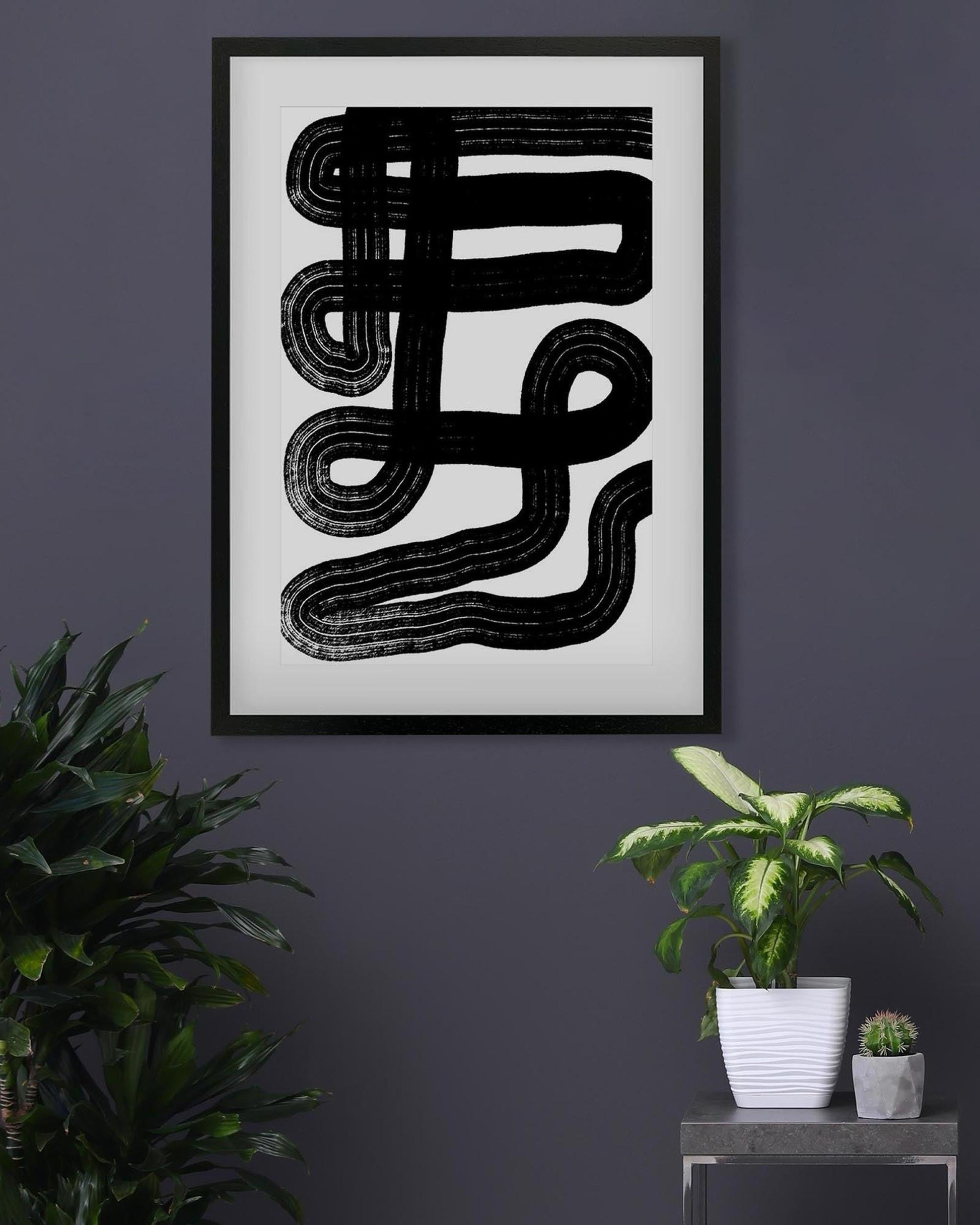Framed abstract black and white artwork on a dark wall with plants below.