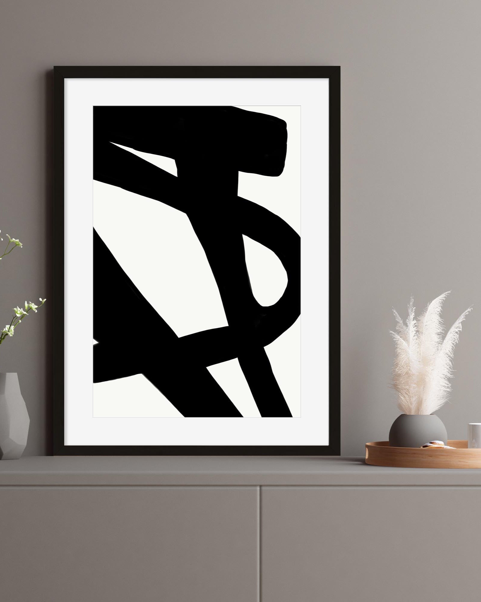 Framed abstract black and white artwork on a gray wall with decorative items below.
