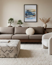 large blue seascape wall art on wall, in modern japandi style living room aesthetic with brown sofa and bespoke ottoman in boucle fabric