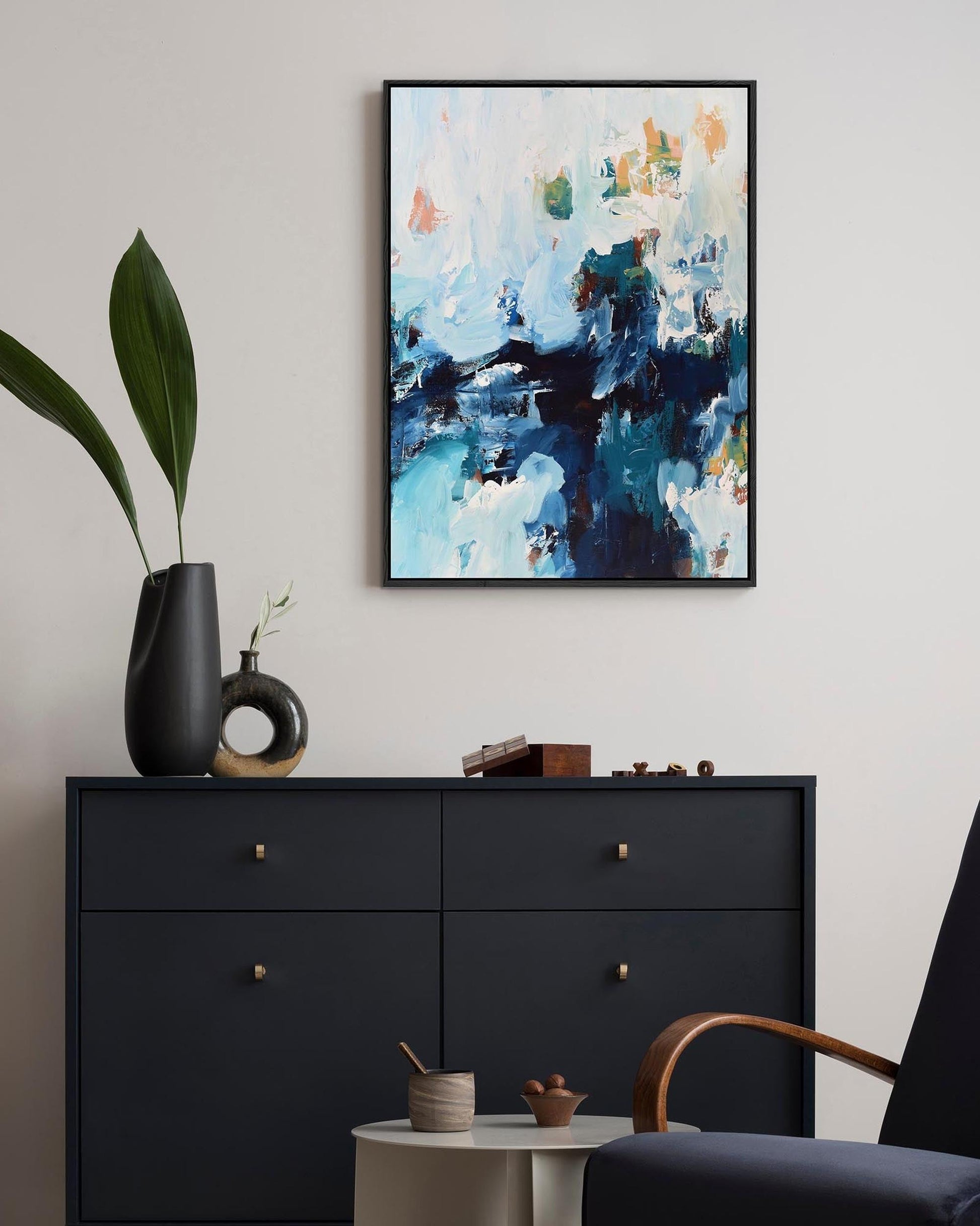 Abstract painting on a wall above a black dresser with decorative items.