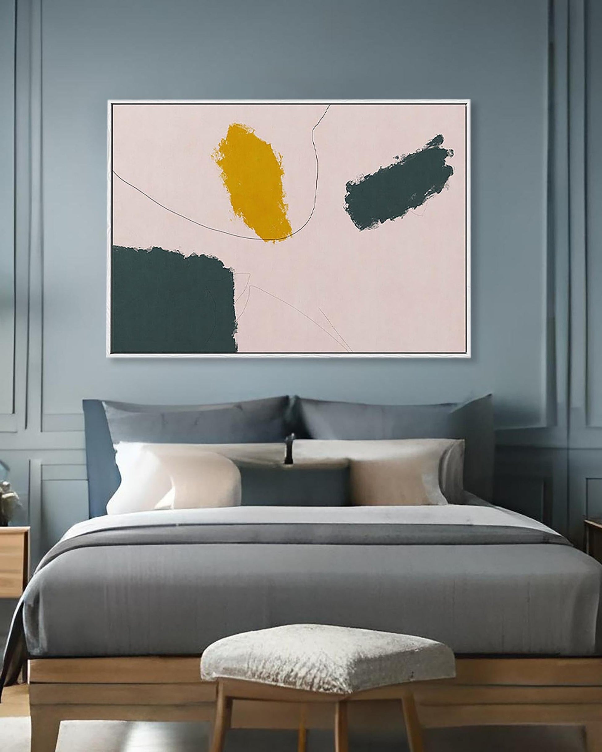 Abstract art piece on a wall above a bed with gray bedding and wooden headboard.